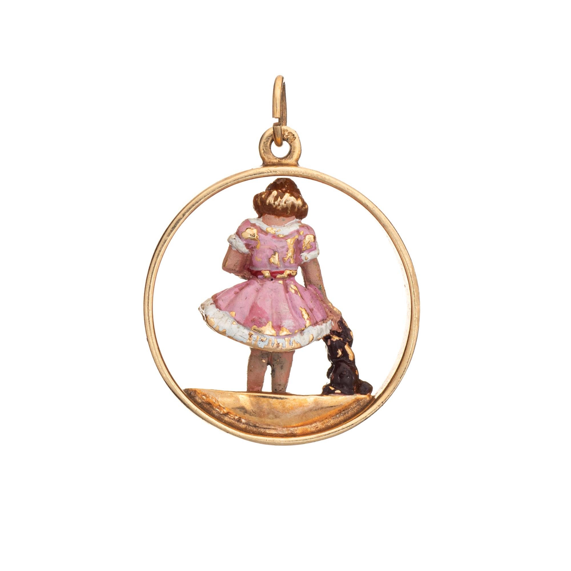Finely detailed vintage charm crafted in 14k yellow gold (circa 1940s to 1950s).  

The finely detailed charm features a young girl holding a toy with her hand comforting a dog. The figure is rendered in pink enamel (note: some loss to the enamel).