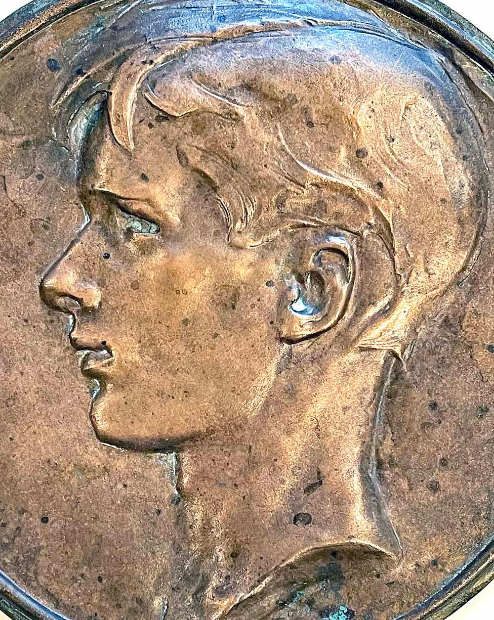 Magnifiquement modelée, coulée et patinée, cette rondelle en bronze représente la tête de profil d'un jeune homme aux cheveux tombant sur le front, au nez fort et à la bouche sensible, probablement sculptée à la fin des années 1920 ou dans les