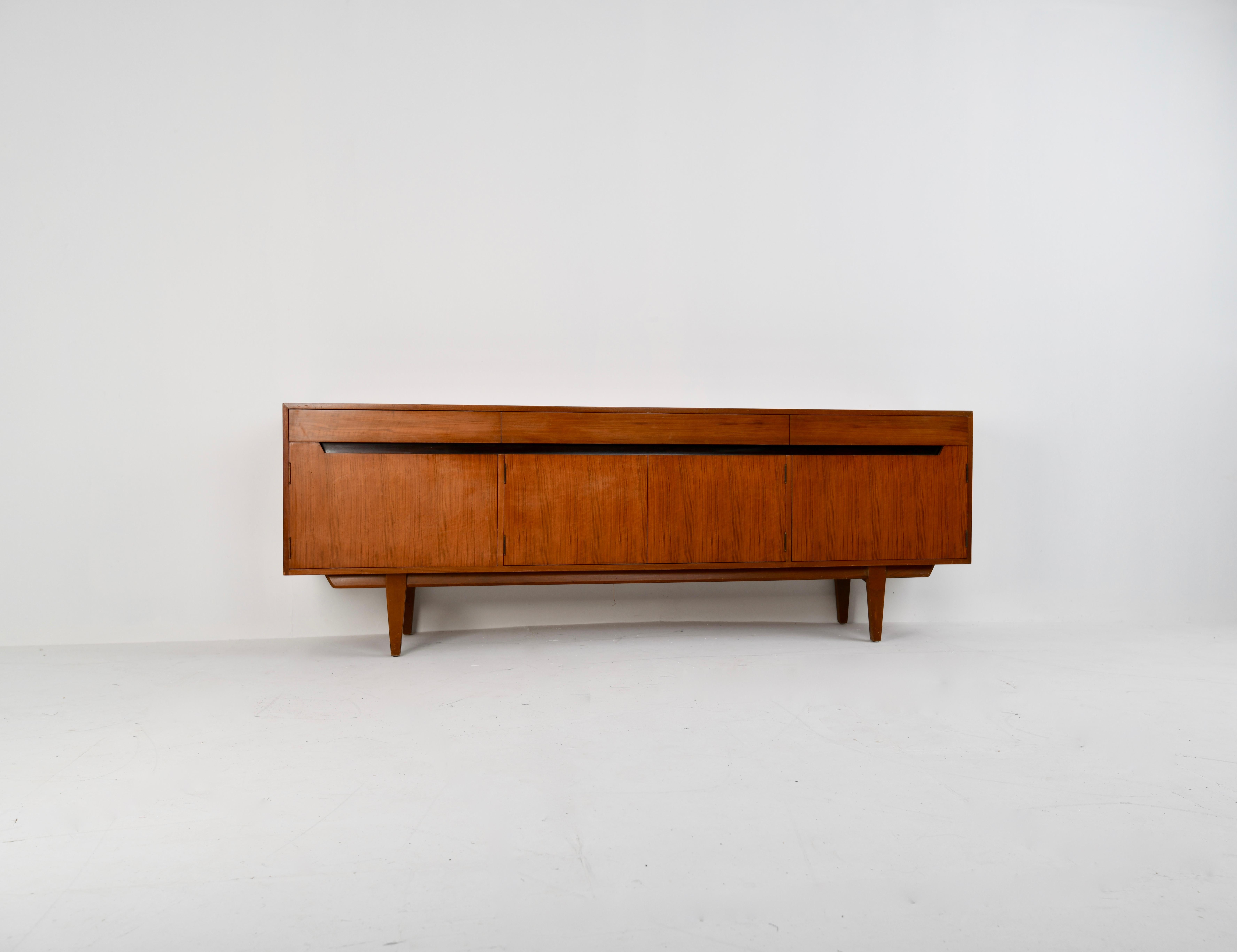 A younger 1960s Minimalist teak and satinwood sideboard, large central drawer and bottom cupboard flanked by a drawer and cuboard, the grain of the satinwood veneers are bookmatched.