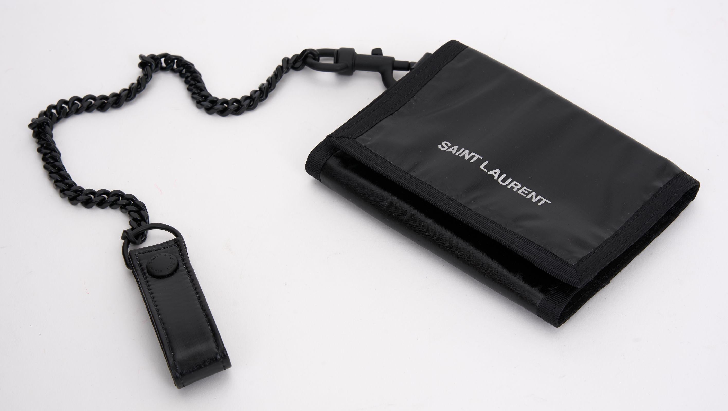 Saint Laurent Chain-Embellished Logo-Print Glossed Nylon Trifold Wallet features a black and silver glossed nylon ripstop, detachable blackened metal chain strap, and interior pockets and slots. You can also clip it to your belt loops. Box and dust