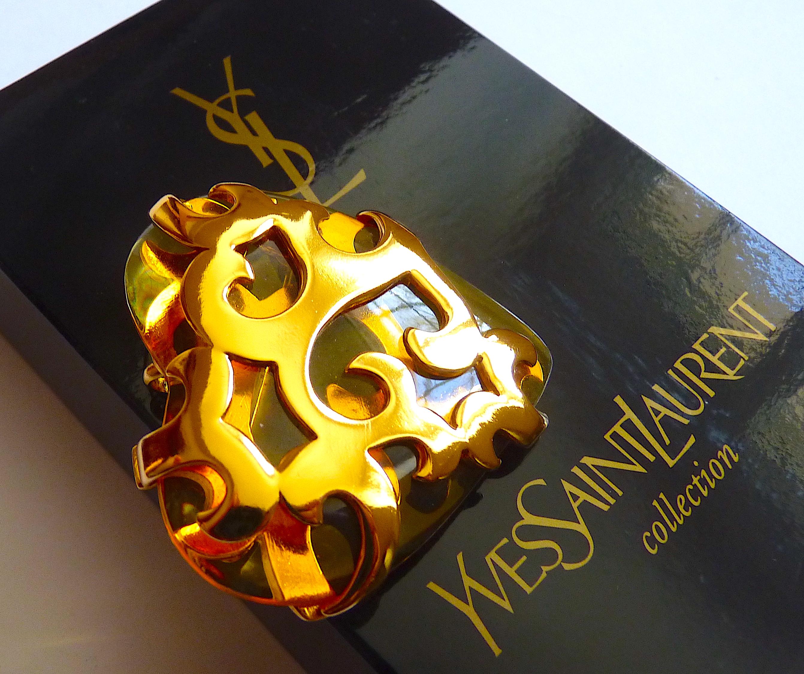 Iconic YSL Brooch Designed By Robert Goossens, Clear Lucite Heart and Gold Plated Metal Arabesques. Vintage from the 80s, can be worn as a Pendant. 
Will come with its complete packaging : black velvet YSL Pouch and Original YSL Box, ready to gift