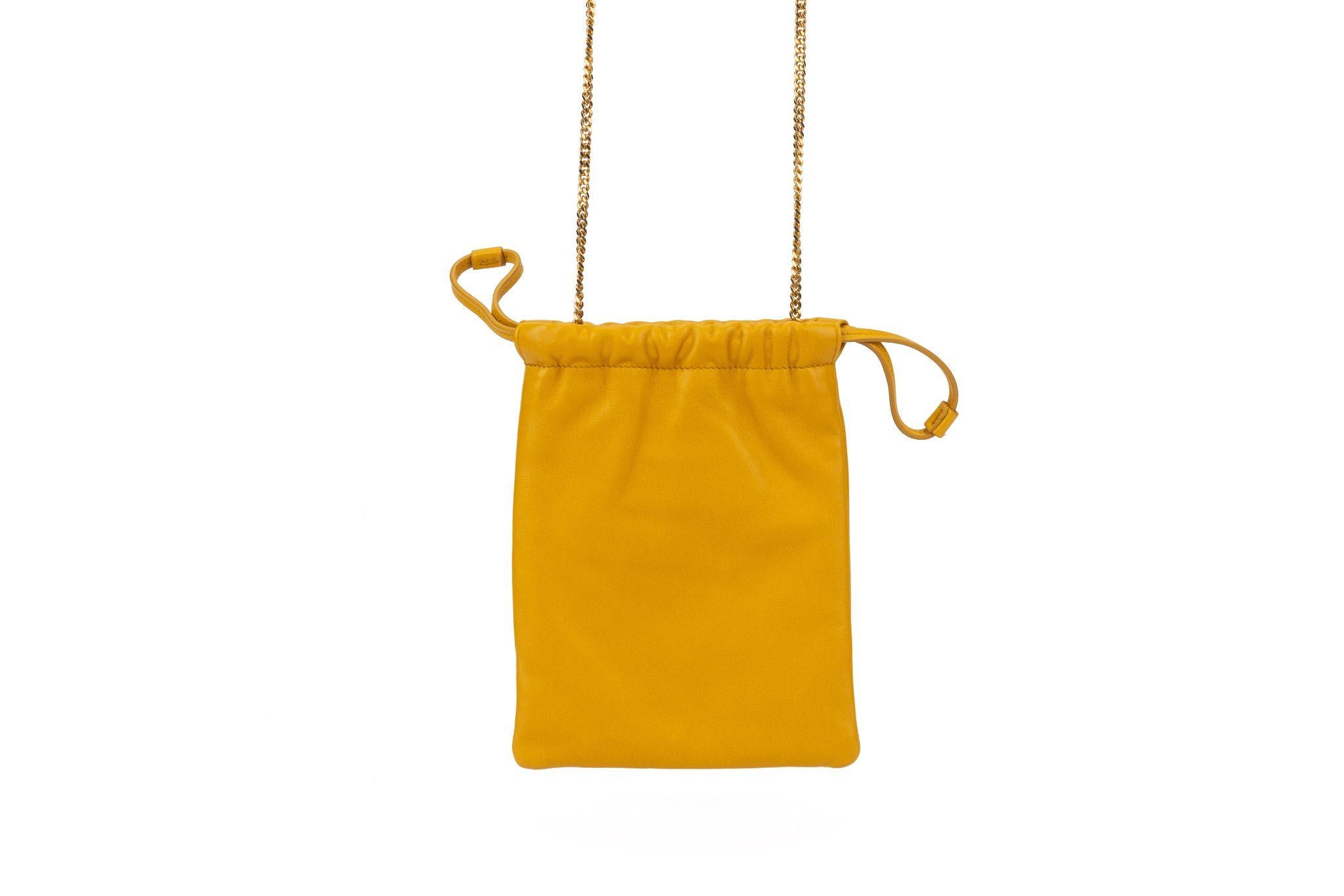 Saint Laurent lambskin bag in shade saffron with gold tone metal hardware chain. It has a drawstring closure and Saint Laurent printed on front. The black cotton interior comes with a brand tag and serial number. Shoulder drop 21.5”. The bag is new