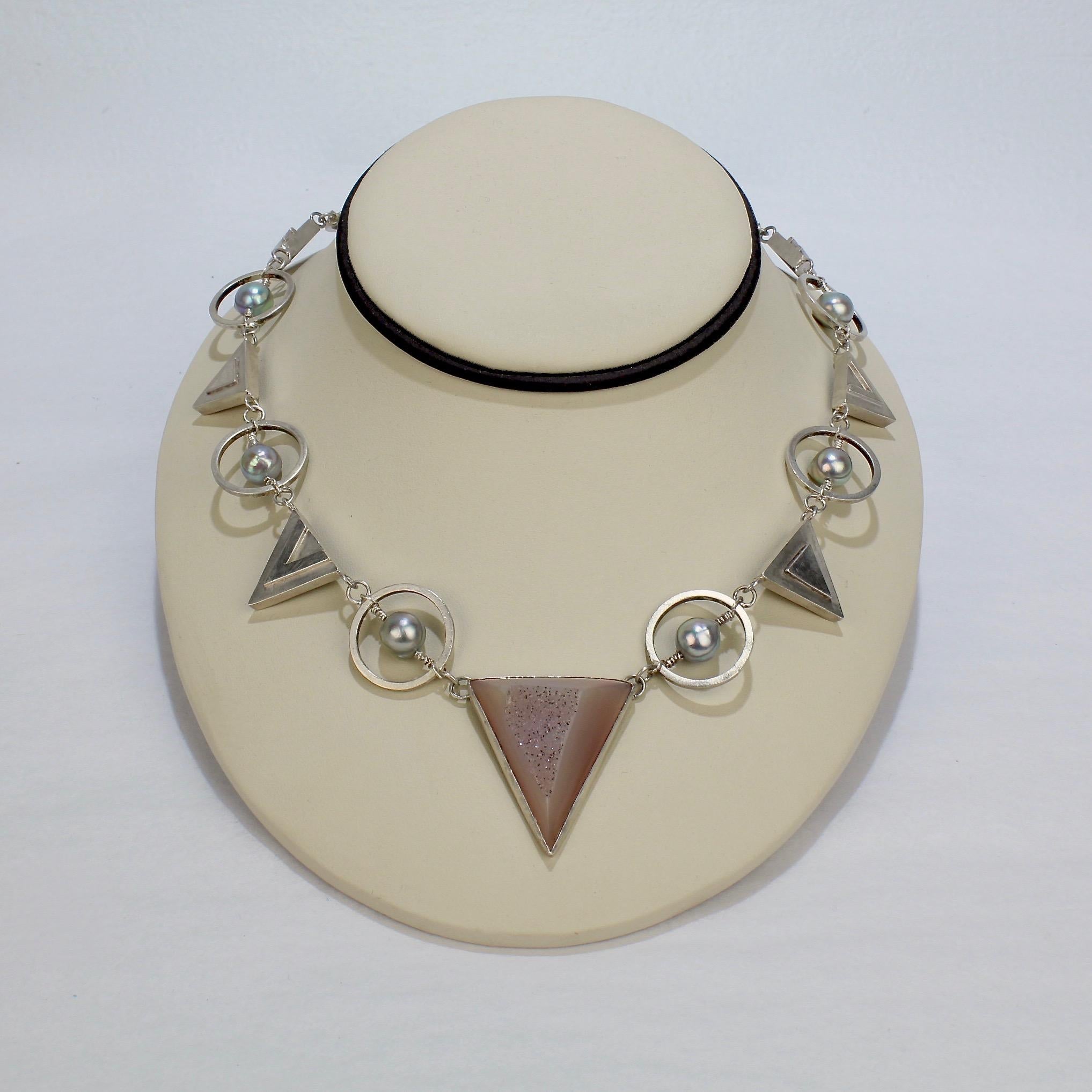 A Retro, geometric necklace and earring parure by Yumi Ueno.  

In sterling silver with alternating triangle and circles centered on a large triangular amethyst druzy pedant. The circle devices are set with grey-blue baroque pearls on twisted wire. 