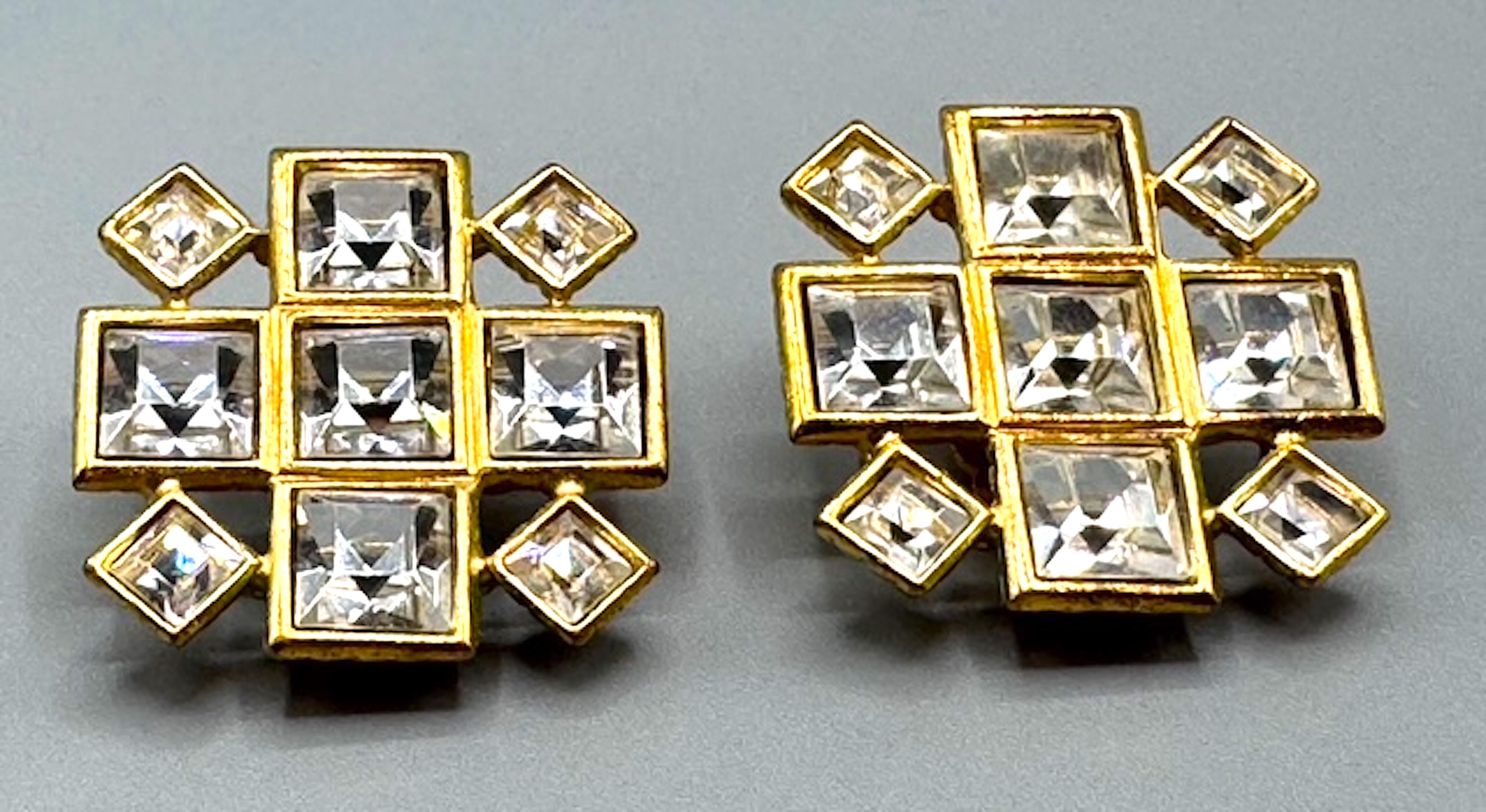 Add a touch of timeless elegance with these exquisite 1990s Yves Saint Laurent clip-on earrings. Featuring a bold cross design in gold-plated metal, each earring is adorned with emerald-cut crystal rhinestones, creating a dazzling statement piece.
