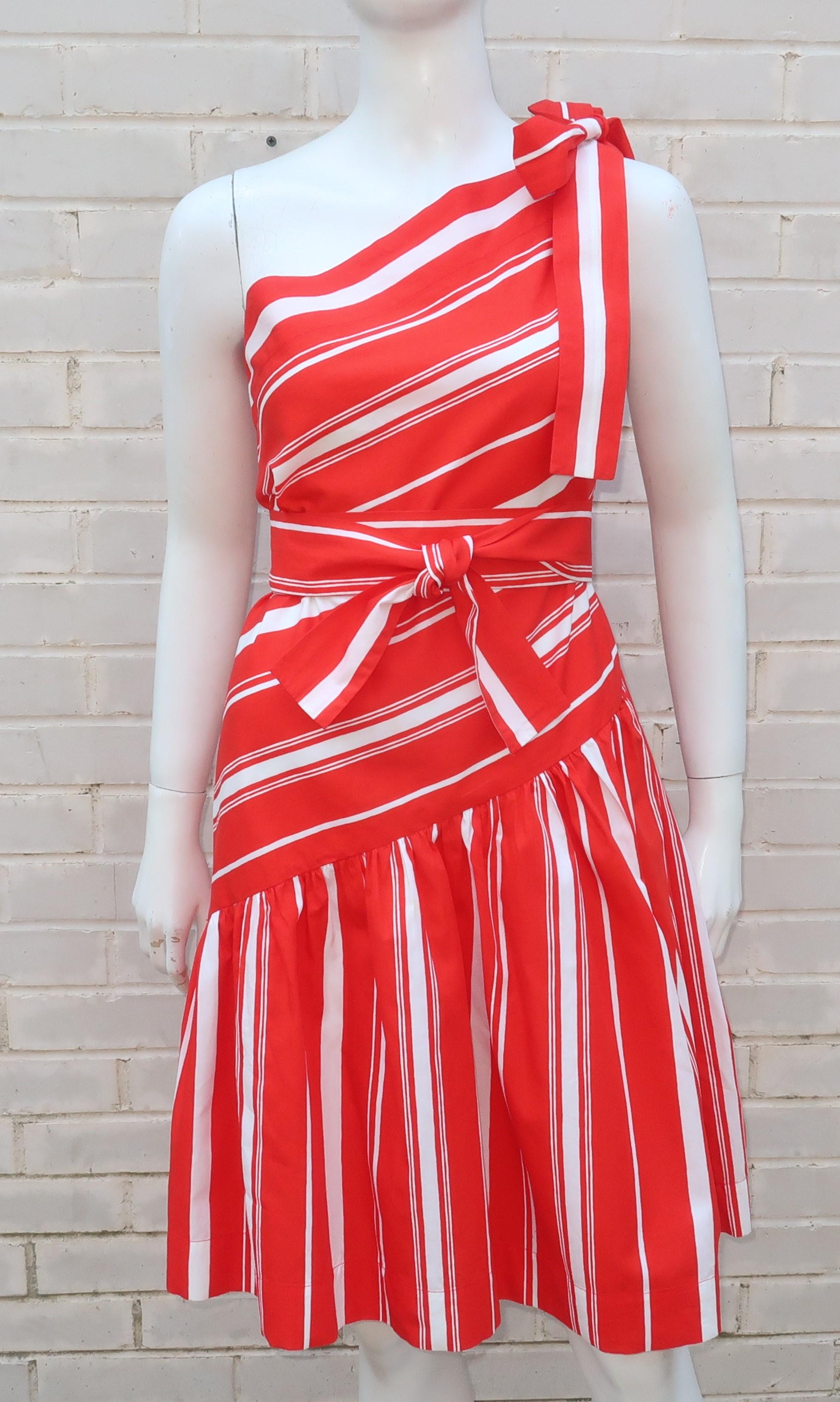 This adorable Yves Saint Laurent red and white candy stripe sundress is a yummy confection.  The crisp cotton fabric features an asymmetrical one shoulder drop waist bodice with a gathered skirt all accented by a tie at the shoulder and another for