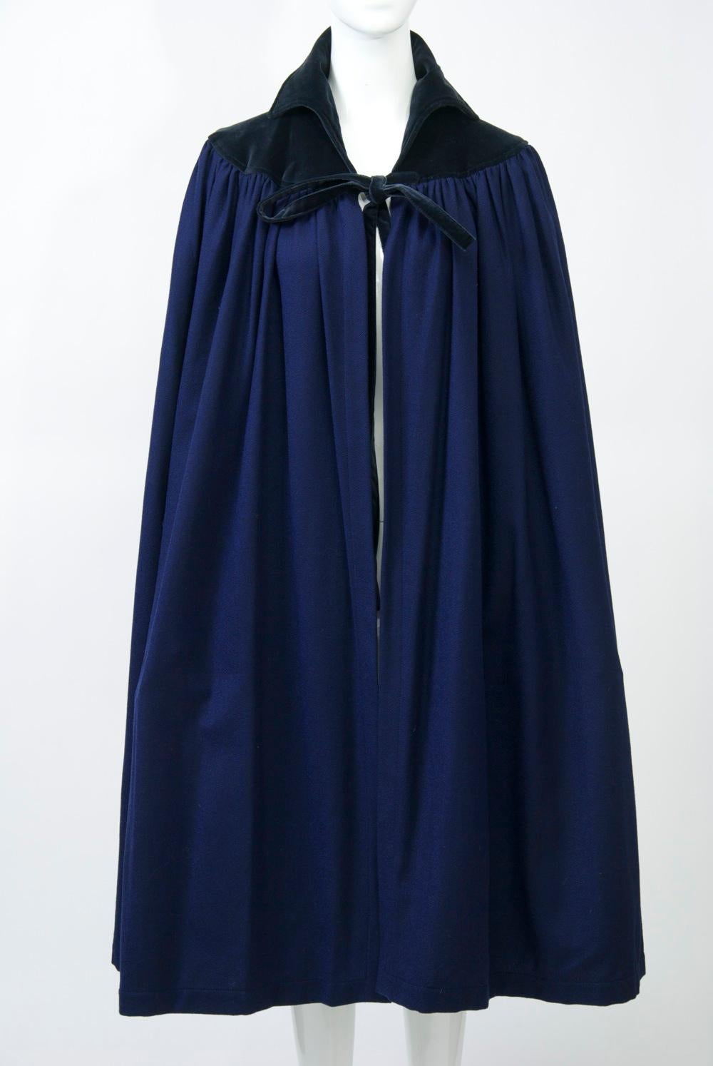 Iconic YSL 1970s Russian Collection cape in dark blue wool with black velvet yoke, collar and tie. The soft wool body is gathered for fullness at the yoke. Mid-calf length. Unlined. A sought-after classic.