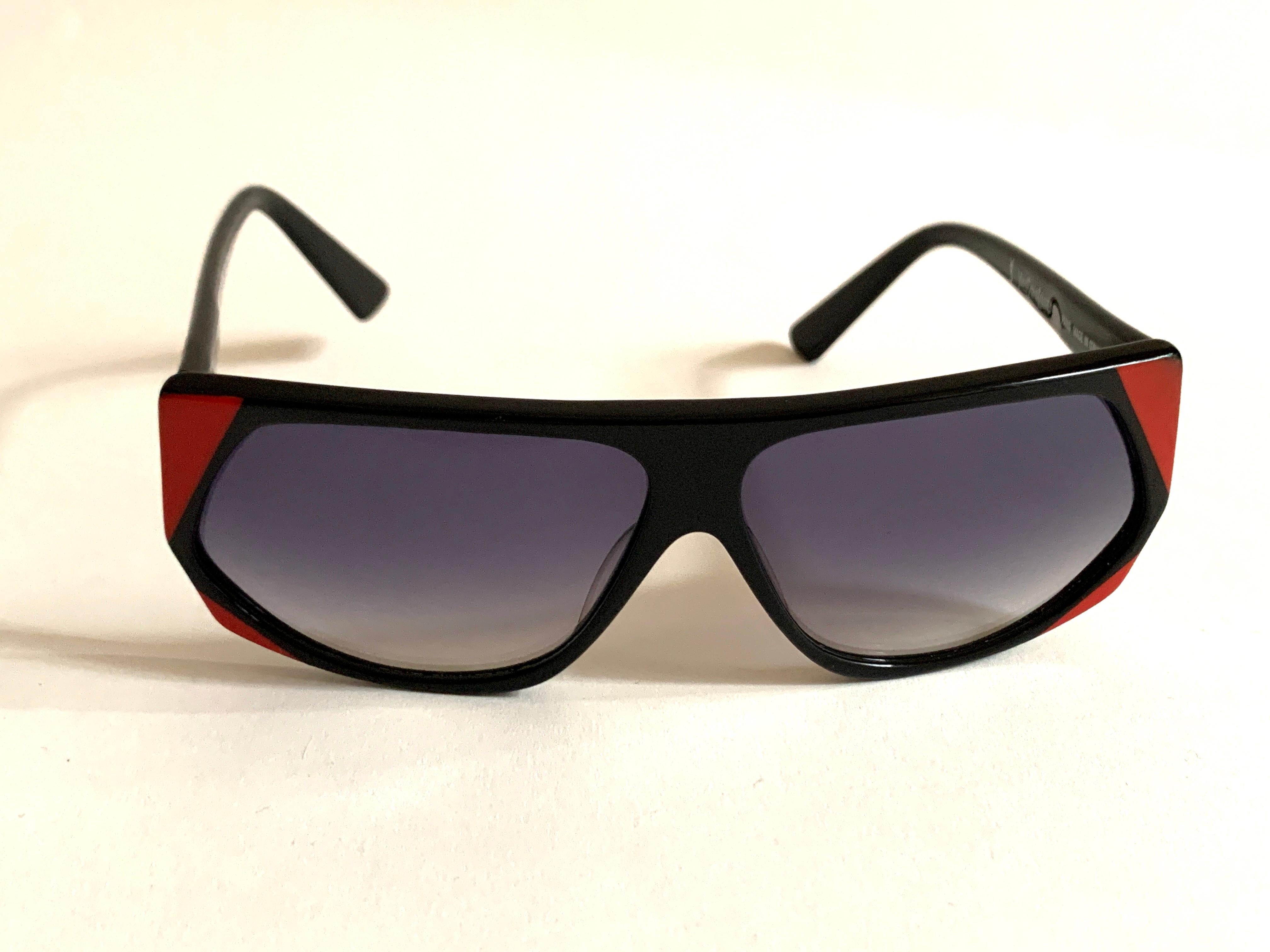 Vintage 1980s Yves Saint Laurent geometric sunglasses in black plastic with red detail at corners and sides. Grey lenses. Gold YSL logo at right temple. From the Museum at FIT.

Frame measures approximately 5 3/8