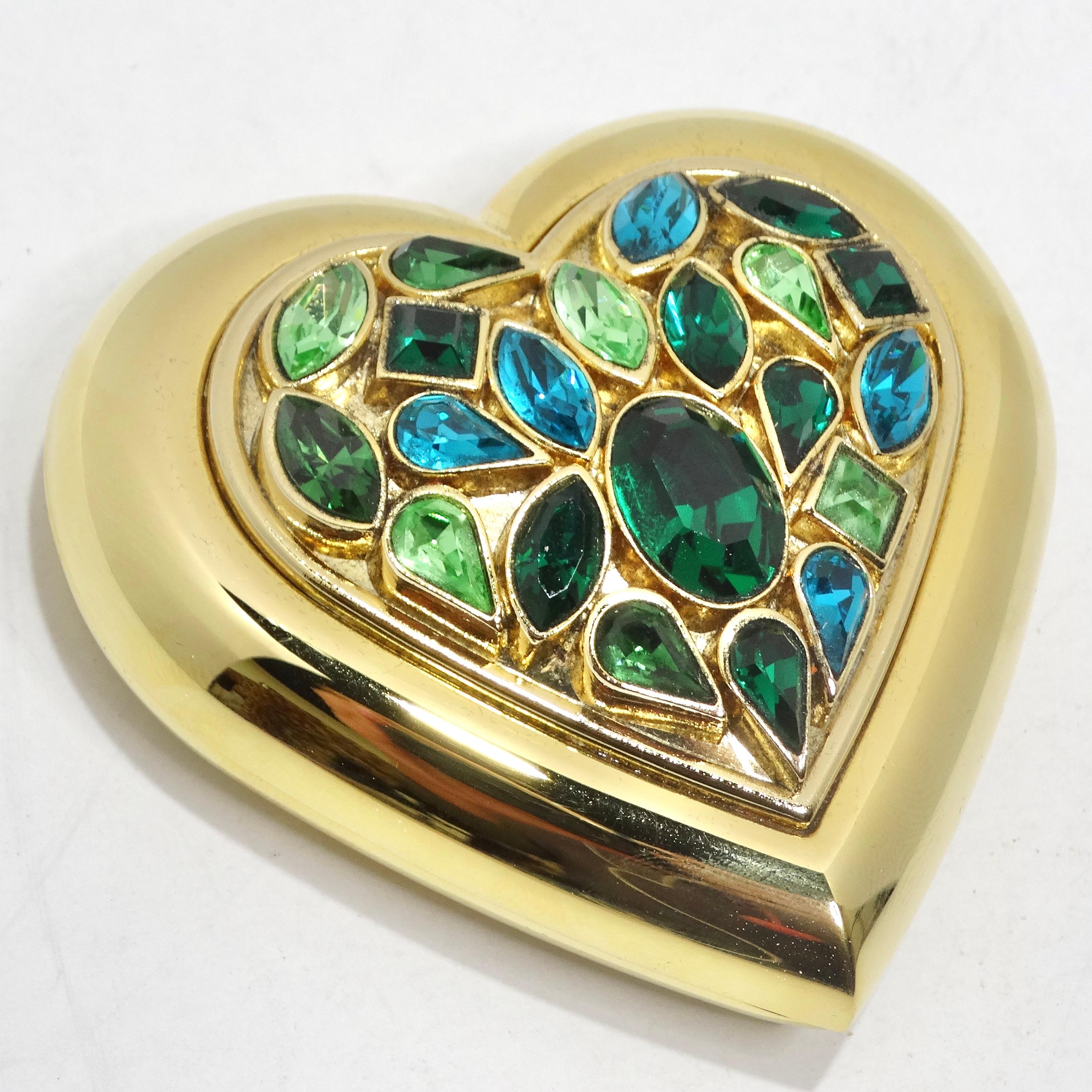 Indulge in vintage elegance with the Yves Saint Laurent 1980s Gem Encrusted Heart Shaped Compact Mirror. This yellow gold plated vanity mirror is designed in the shape of a heart and features a plethora of blue and green gems on the front, elevating