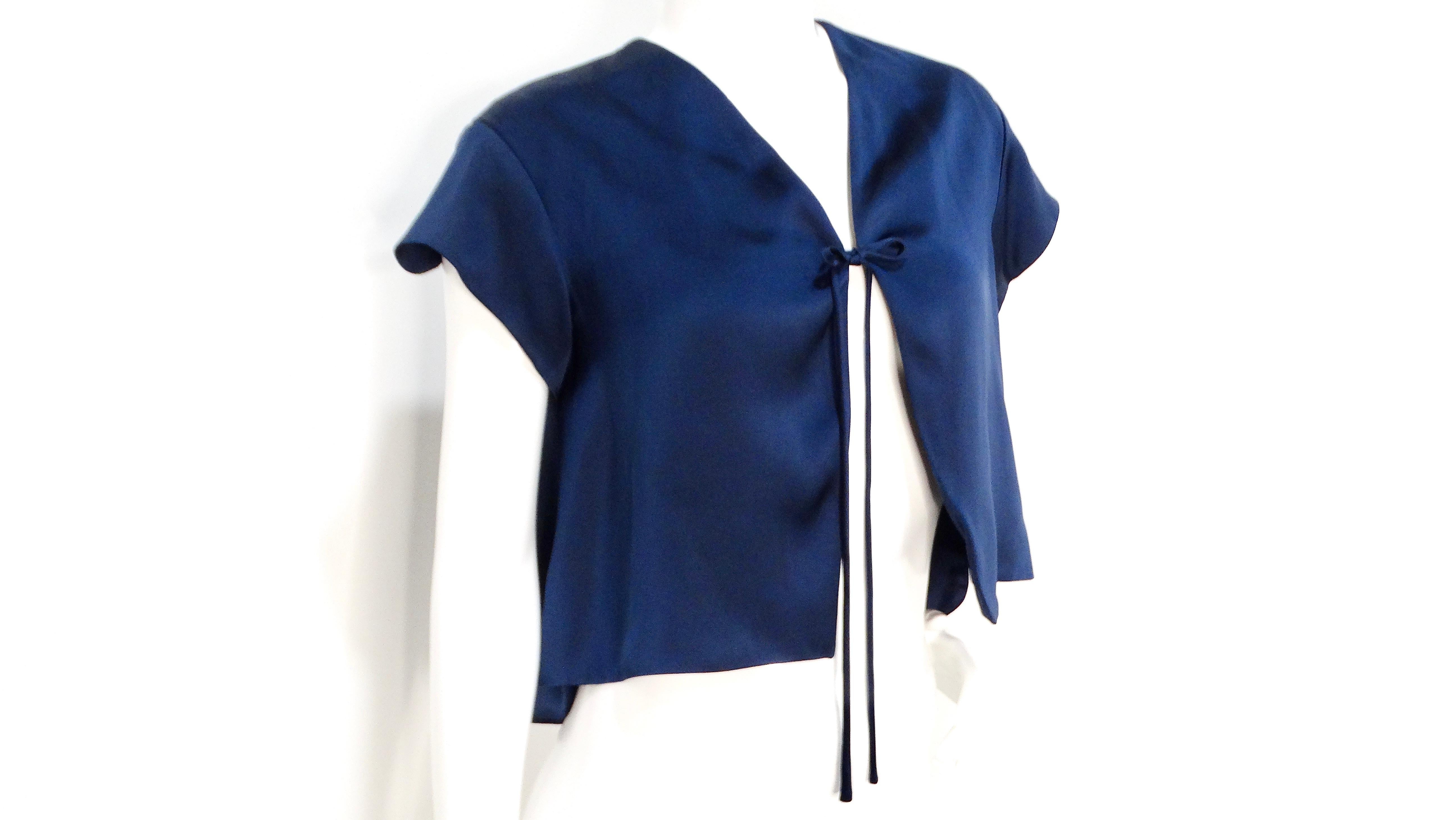 The Yves Saint Laurent 2008 Navy Silk Tie Cropped Blouse is a stunning piece that effortlessly combines sophistication and modern design. Crafted from luxurious 1100% silk, this blouse features a unique bow tie closure in the front, adding a playful