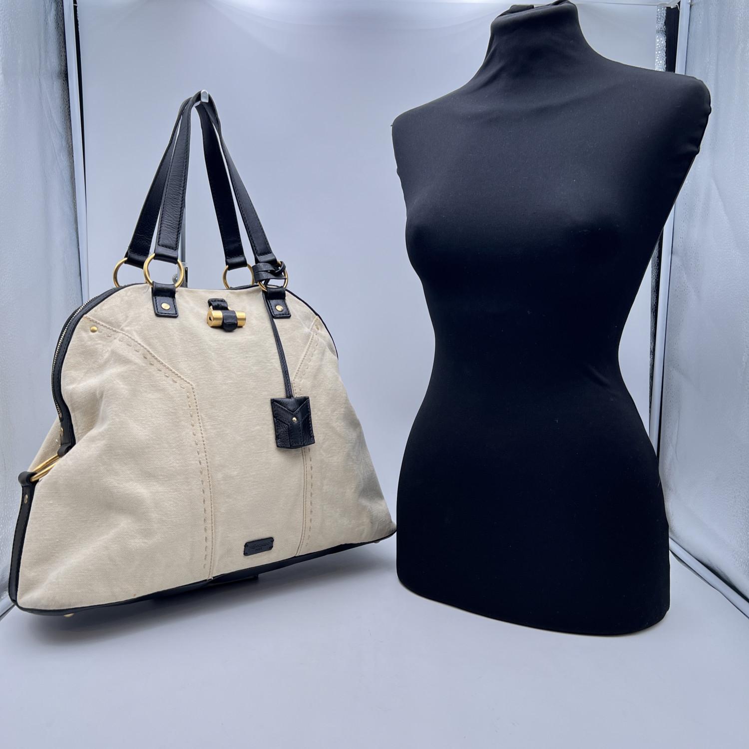 Iconic YVES SAINT LAURENT 'Large Muse bag' in beige canvas with black leather trim and handles. The bag features gold metal hardware, whip stitching and the iconic Muse padlock detailing on the front (Keys are included). The upper zipper closure
