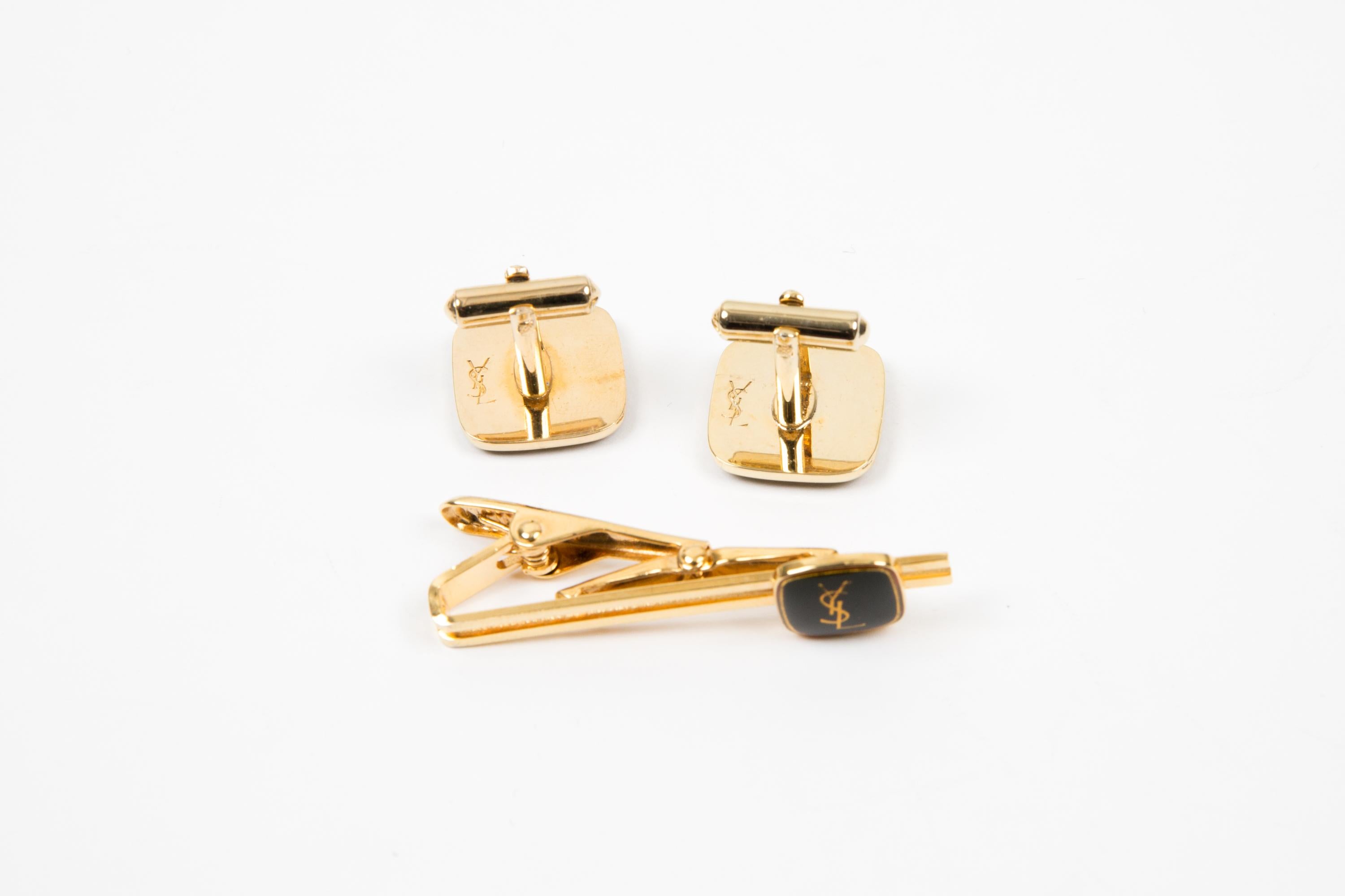 Yves Saint Laurent black Cassandre-logo YSL  tie clip and cufflinks set featuring a square shape, a black ground, a center gold-tone YSL. They come as a pair + a tie accessory.  
In good vintage condition Circa 1990s  
Cufflinks:
Maxi Length: 0.6 in