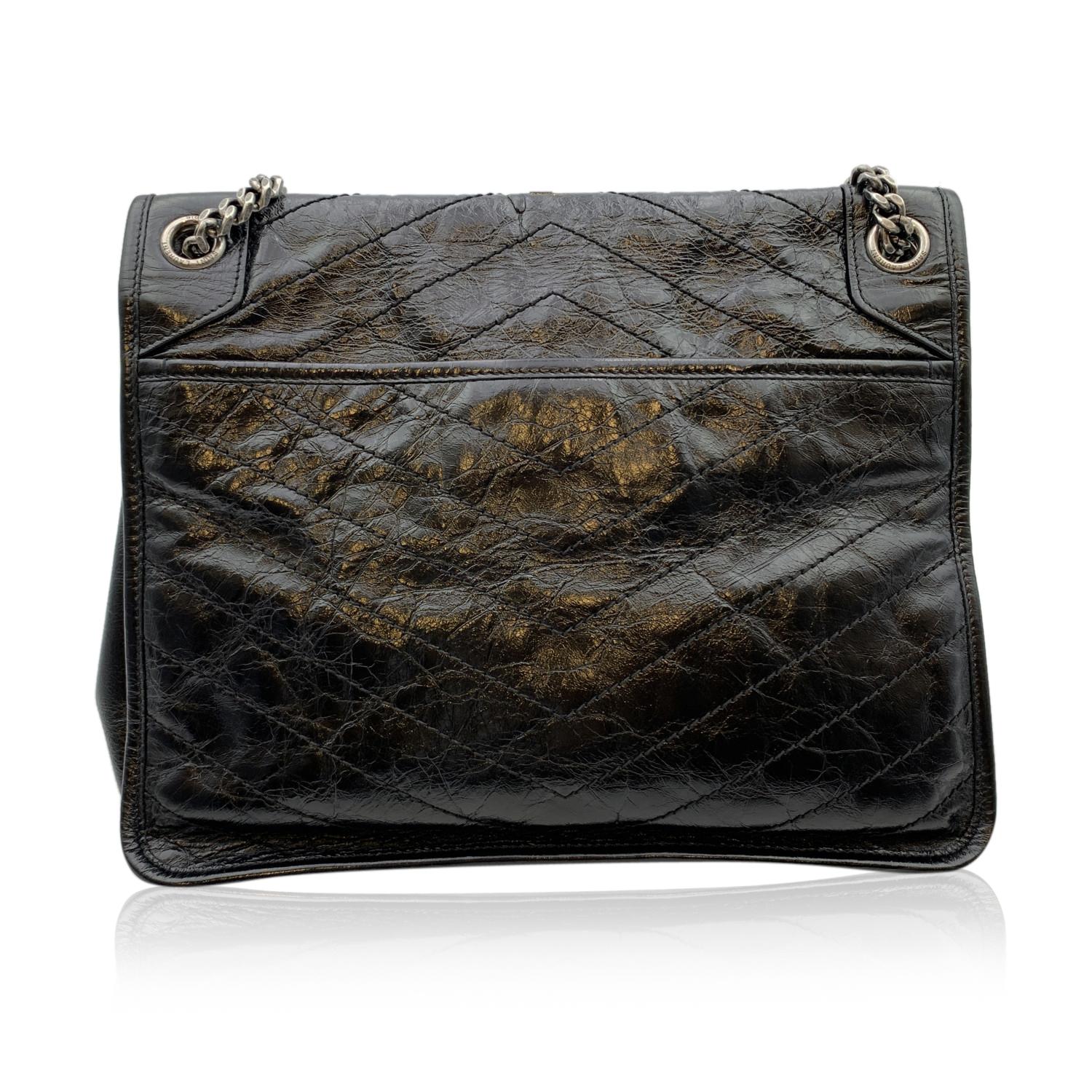 Iconic YVES SAINT LAURENT 'Niki' in black chevron quilted crinkled leather. The bag features a front flap with magnetic button closure, black metal YSL logo on the front, leather and antiquated silver metal chain shoulder strap. Black gros-grain