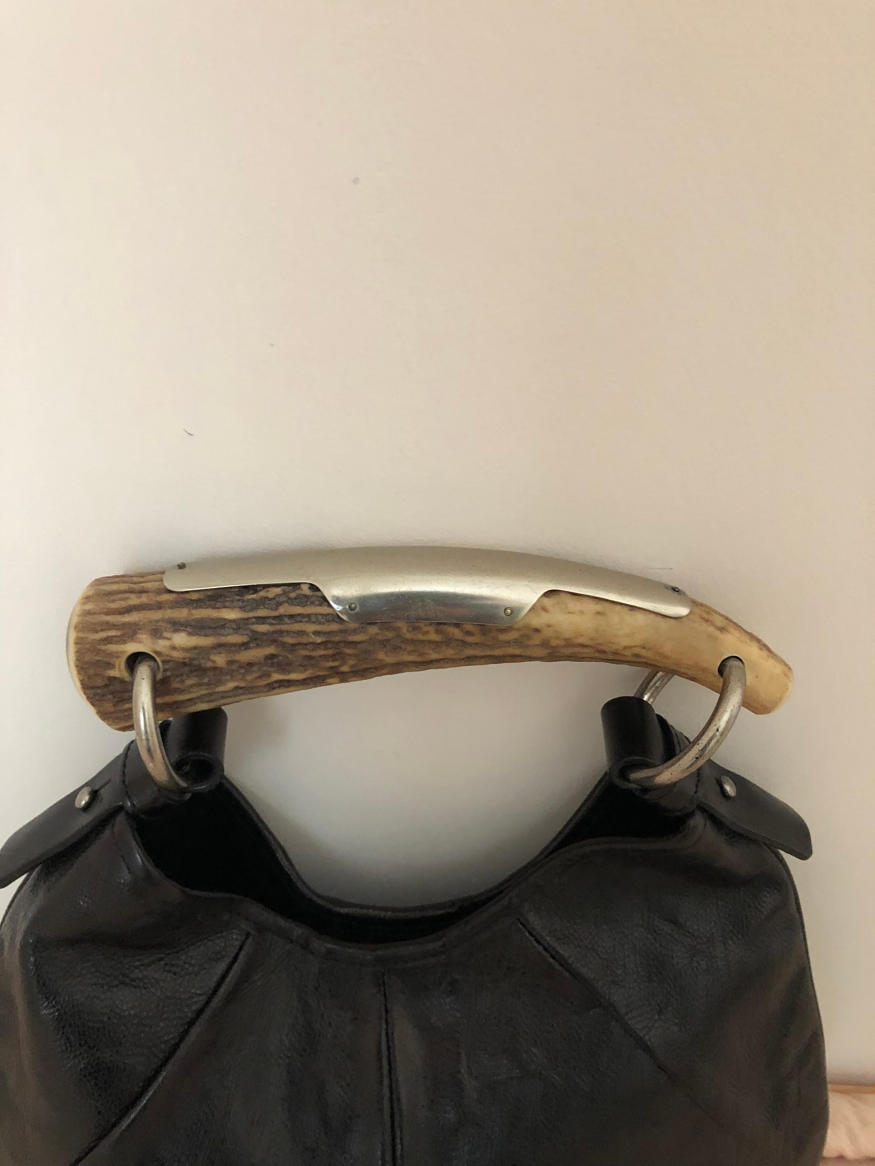 This is an early 2000s Tom Ford for Yves Saint Laurent black textured caviar leather hobo handbag, with a deer horn silver trimmed handle. It has a black suede lined interior with a patch pocket and a snap closure at top.
The bag was made in Italy
