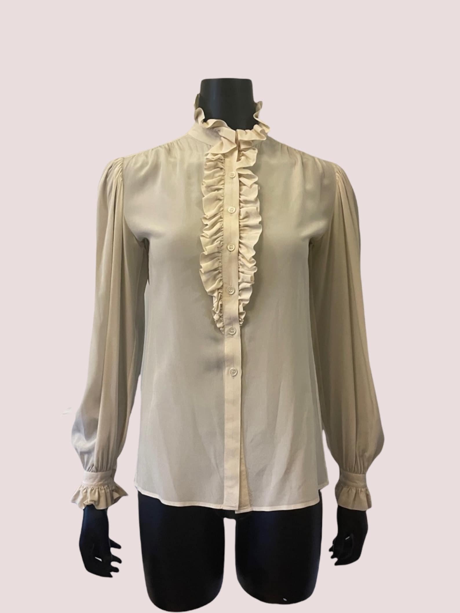 Yves Saint Laurent knochenbeige Seidenbluse. Rüschenkragen, Knopfleiste und Manschetten im Jabot-Stil. Lange Ärmel. Knopfverschluss vorne. Chemisch gereinigt.

Circa 1970er Jahre
Yves Saint Laurent Rive Gauche
Hergestellt in Frankreich
Markiert eine