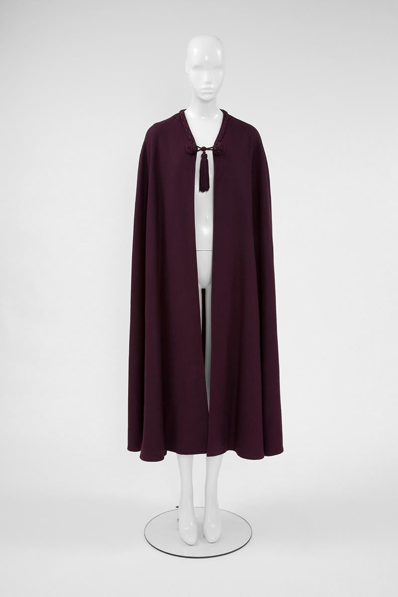 Cut in a sweeping silhouette, this rare YSL 70's eggplant wool cape drapes effortlessly from the shoulders, while a matching color braid embellishes the neckline. Tassel and braided toggle fastening. Unlined. Iconic and timeless piece that can be
