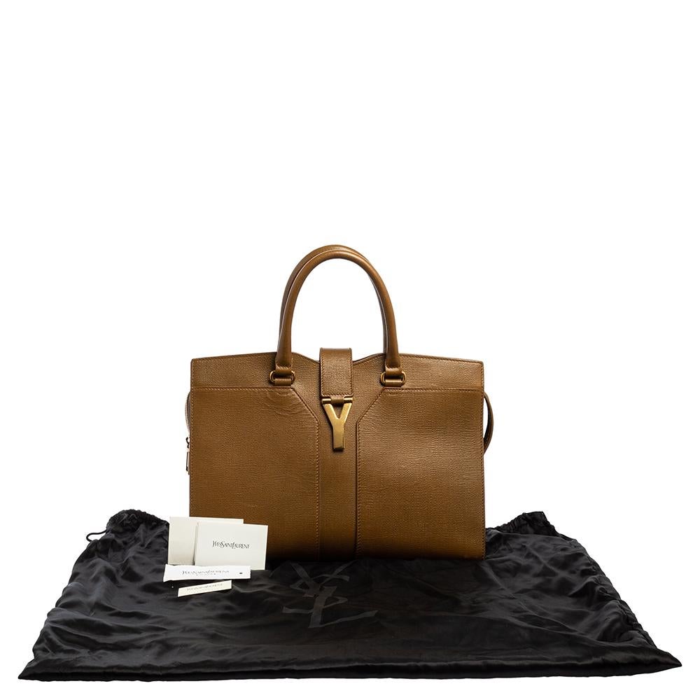 This elegant brown Cabas Chyc tote from Saint Laurent is ideal for everyday use. Crafted from leather, the bag is detailed with a gold tone hardware Y motif snap closure and dual-rolled handles. The top zip closure opens to a spacious interior that