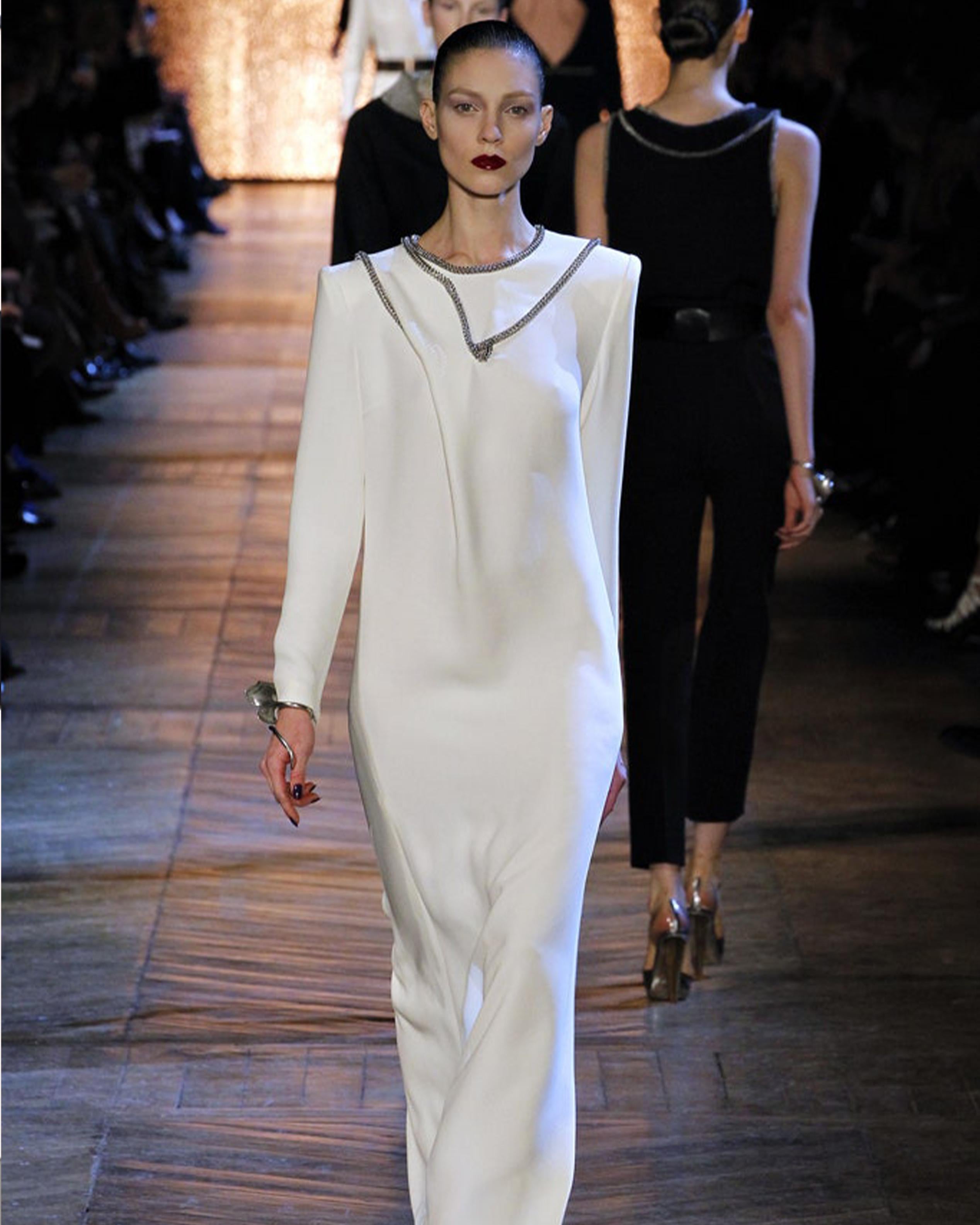 - Designed by Stefano Pilati
- Fall Winter 2012 Collection
- Runway Piece
- Cream embellished long dress
- Features a striking silhouette with long sleeves and floor-length cut
- Adorned with distinctive silver chain mail trim in an intricate