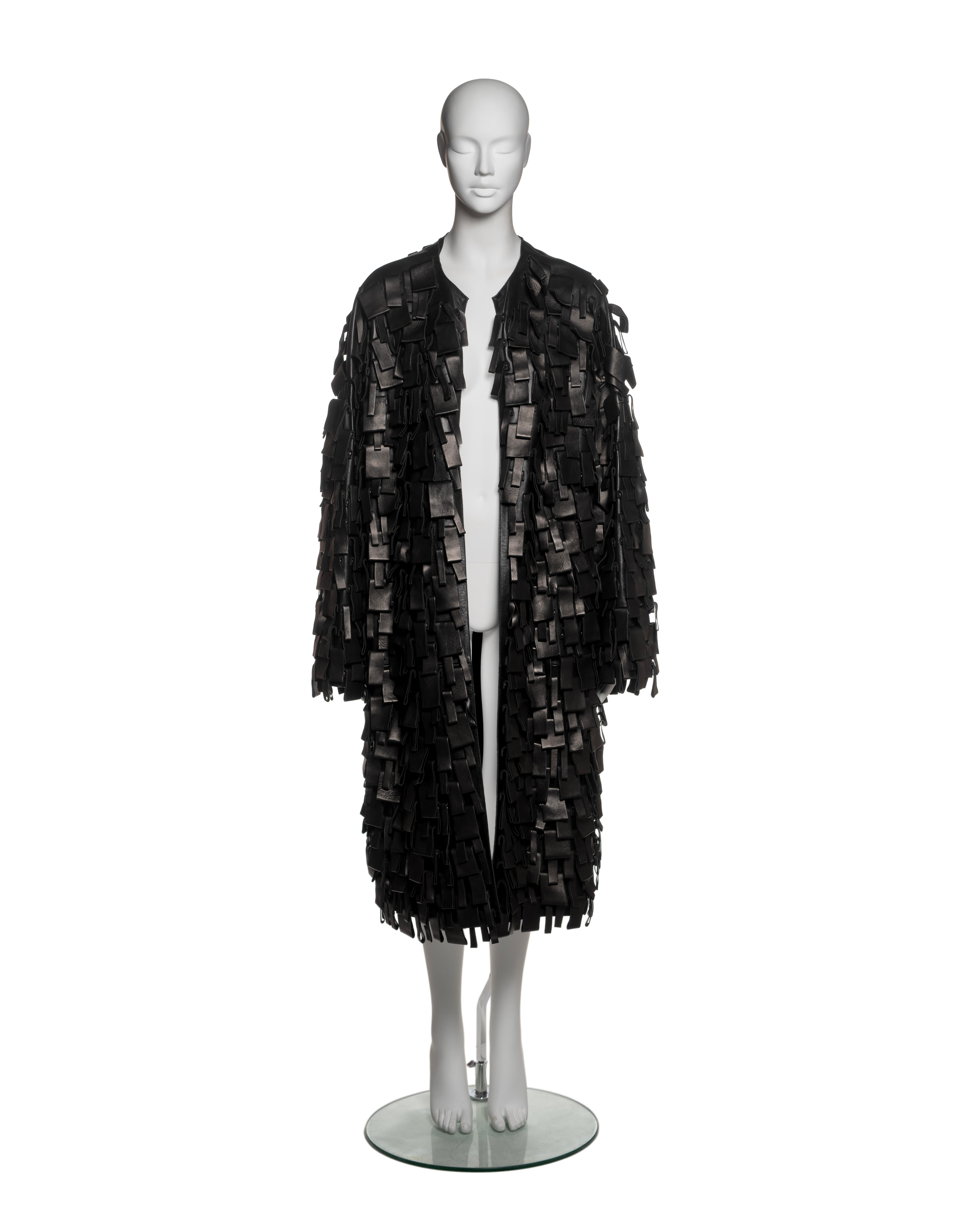 This Yves Saint Laurent by Tom Ford coat from the Fall-Winter 2002 collection is constructed from black leather and features an open-front design with a straight, oversized silhouette. The coat is fully embellished with layered rectangular leather