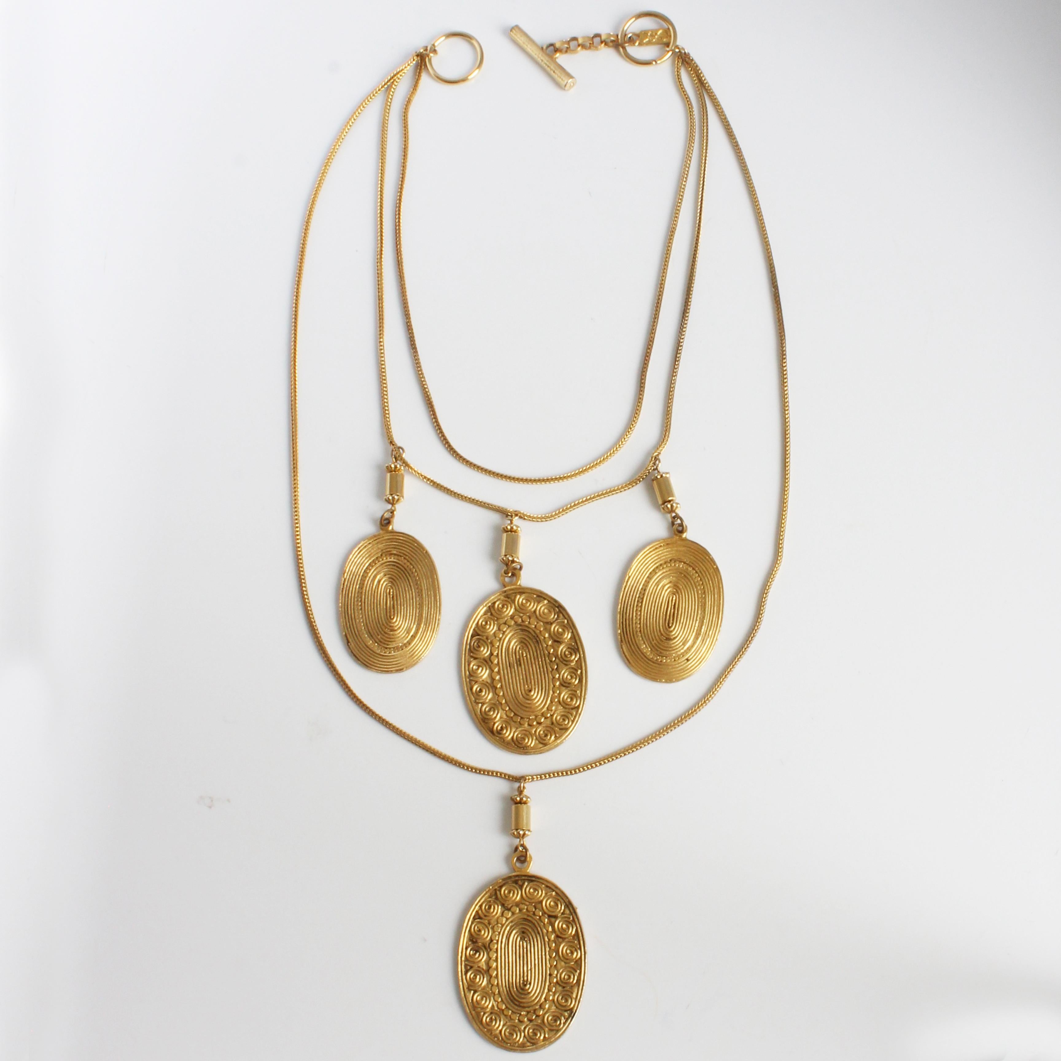 Vintage coin or medallion necklace, made by Yves Saint Laurent, most likely in the late 70s. Made from gold metal, it features three chain strands with a total of four dangling medallions.  Each Etruscan-style medallion features a swirl pattern on