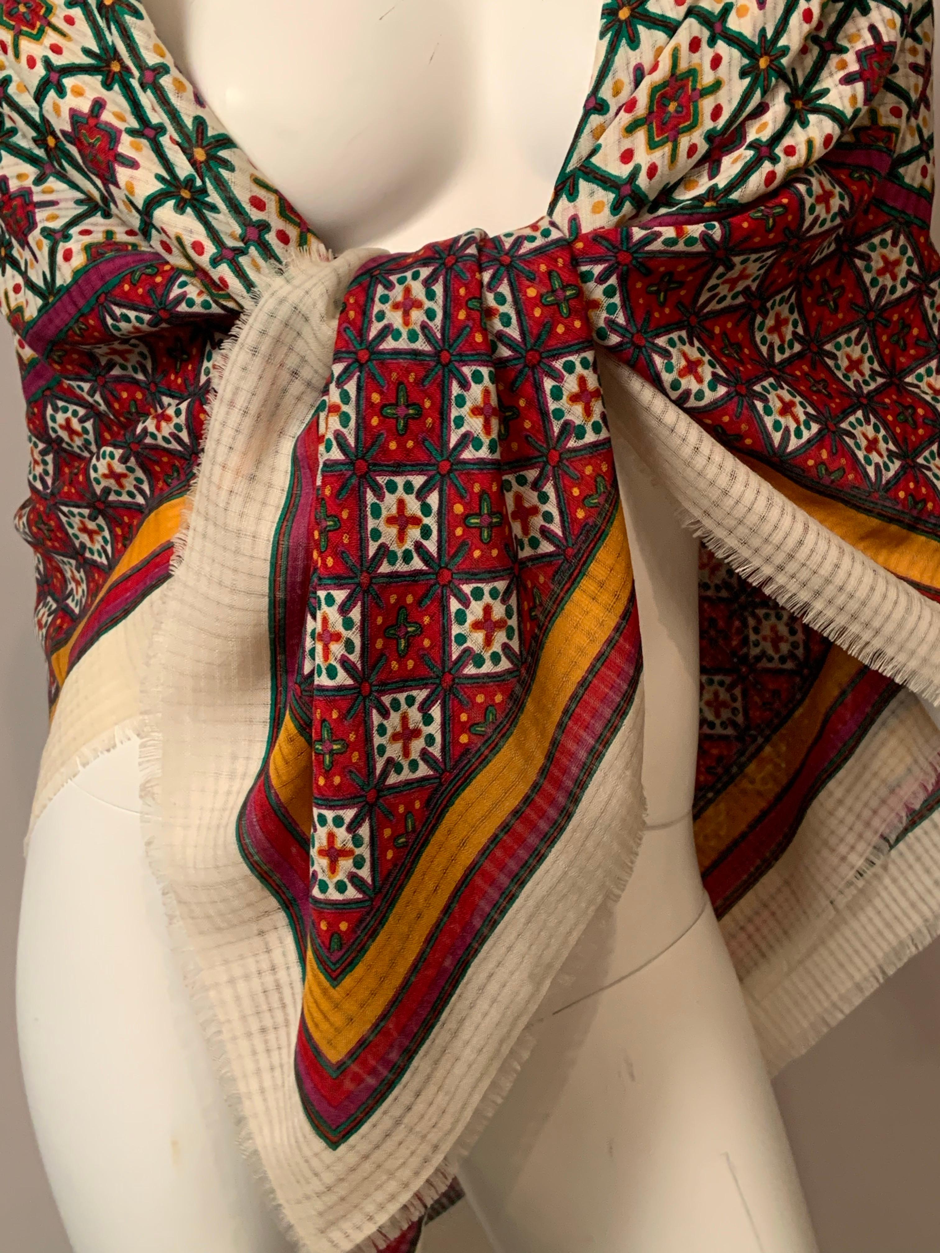 Questo scialle in lana challis di Yves Saint Laurent è pieno di colori!  Il centro dello scialle ha uno sfondo bianco con disegni in magenta, verde e giallo.  Il tutto è orlato da un sottile bordo verde e viola.  Poi c'è un'ampia fascia rossa con