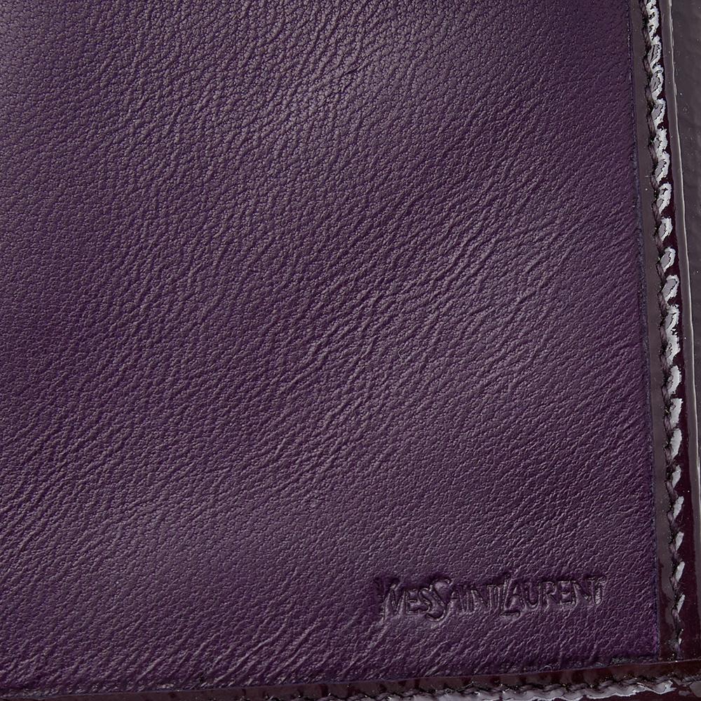 Keep all your belongings safe and stylish by carrying this long wallet from the House of Yves Saint Laurent. It is made from dark-purple patent leather on the exterior with a gold-toned accent perched on the front. It comes with a nylon-lined