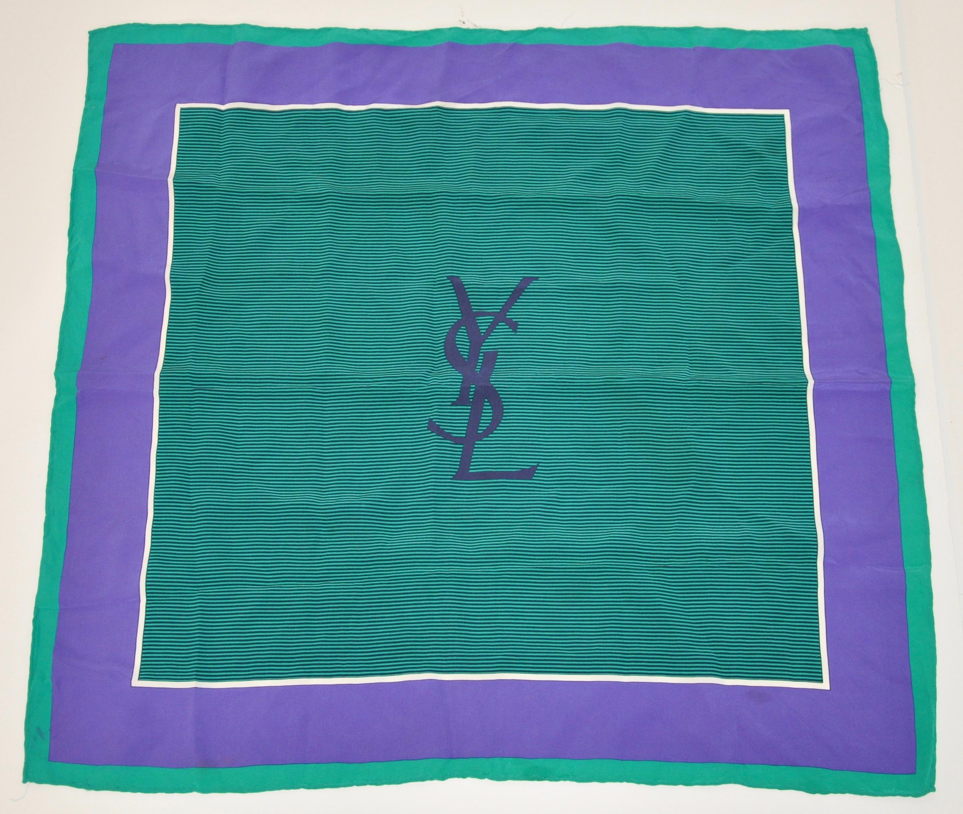        L'écharpe en soie à bordure verte et lavande profonde signée Yves Saint Laurent, avec des bords roulés à la main, mesure 24 pouces sur 25 pouces. Fabriqué en France.
