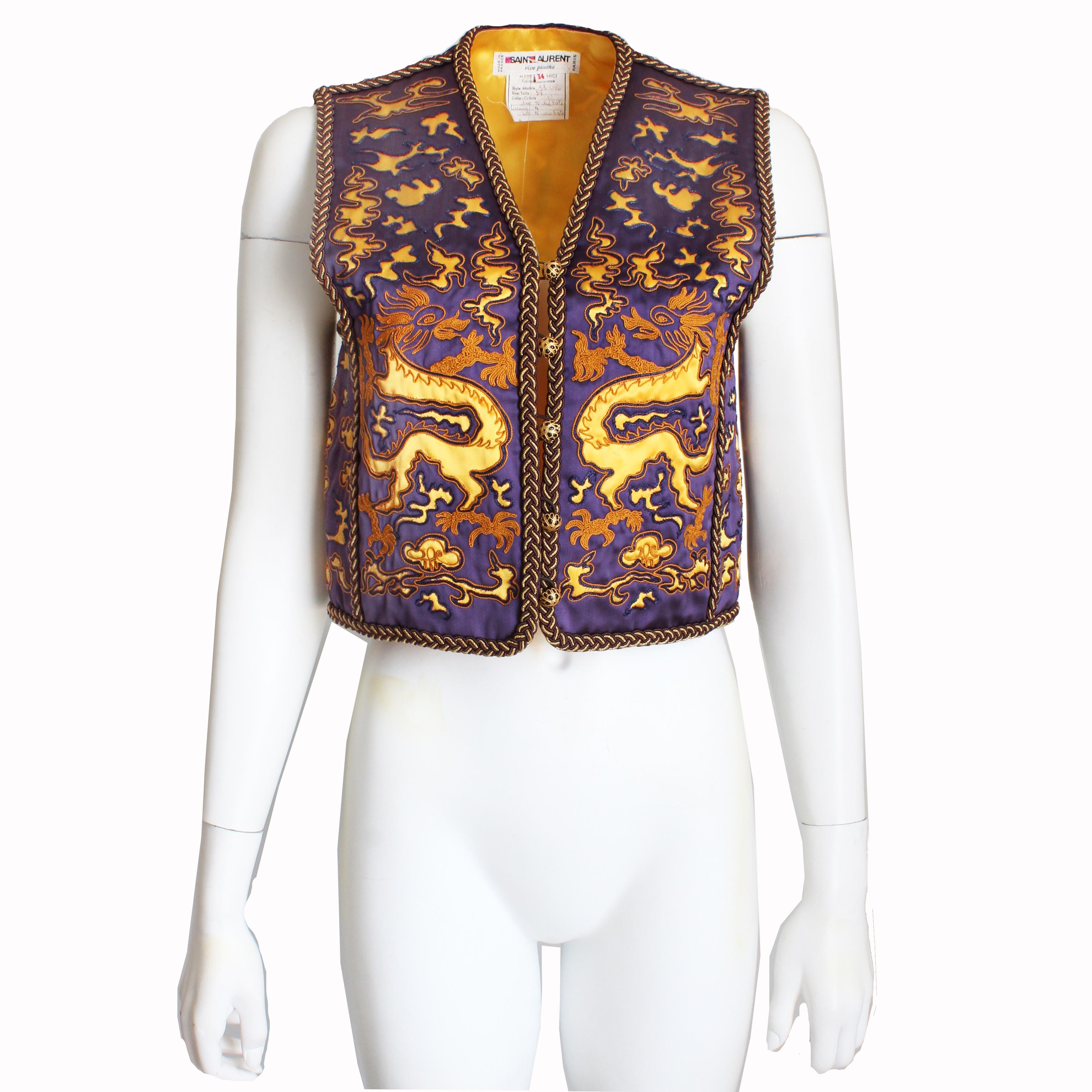Vintage Yves Saint Laurent dragon vest, likely made in the late 60s or early 70s.  Made from a rich purple fabric, it features abstract golden dragon shapes with embroidery throughout and is trimmed in brown and gold braiding.  It fastens with five