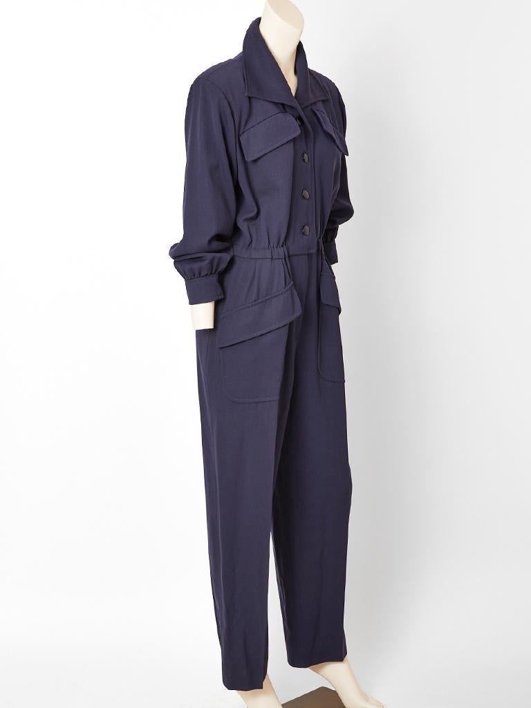 Yves Saint Laurent, Rive Gauche, navy, wool gabardine,  long sleeve, jumpsuit, having a large pointed collar, Jet buttons, front closure to the waist, breast and hip flap pockets and an elastic at the waist.
Designed to be worn with a belt so the