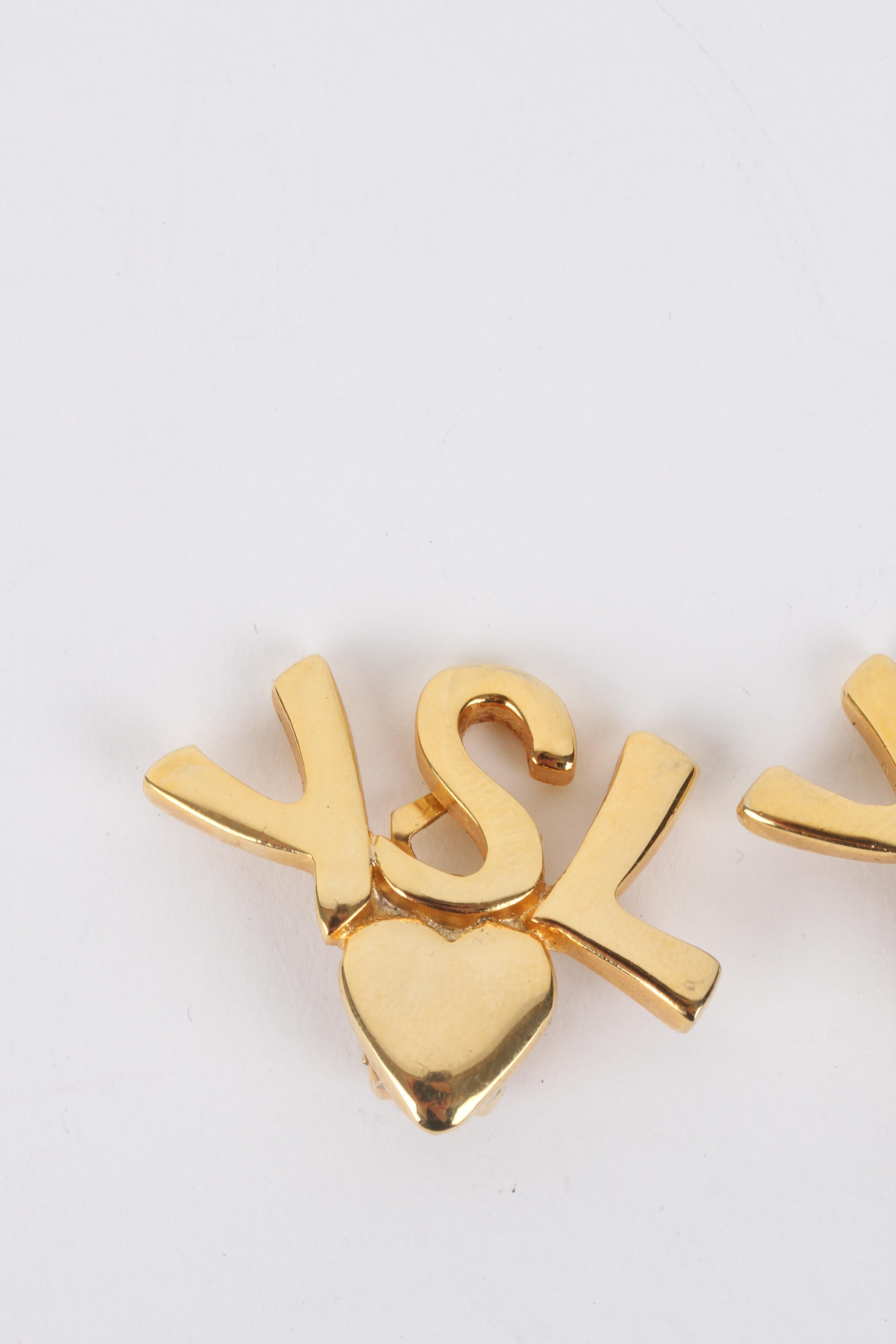 Yves Saint Laurent Gold Logo Initials Heart Clip-On Earrings.

These earrings feature a lux gold-coloured 'YSL'-logo exterior with a smaller bottom heart finish. The earrings feature a gold-plated backside clip fastening. The exterior is clean and