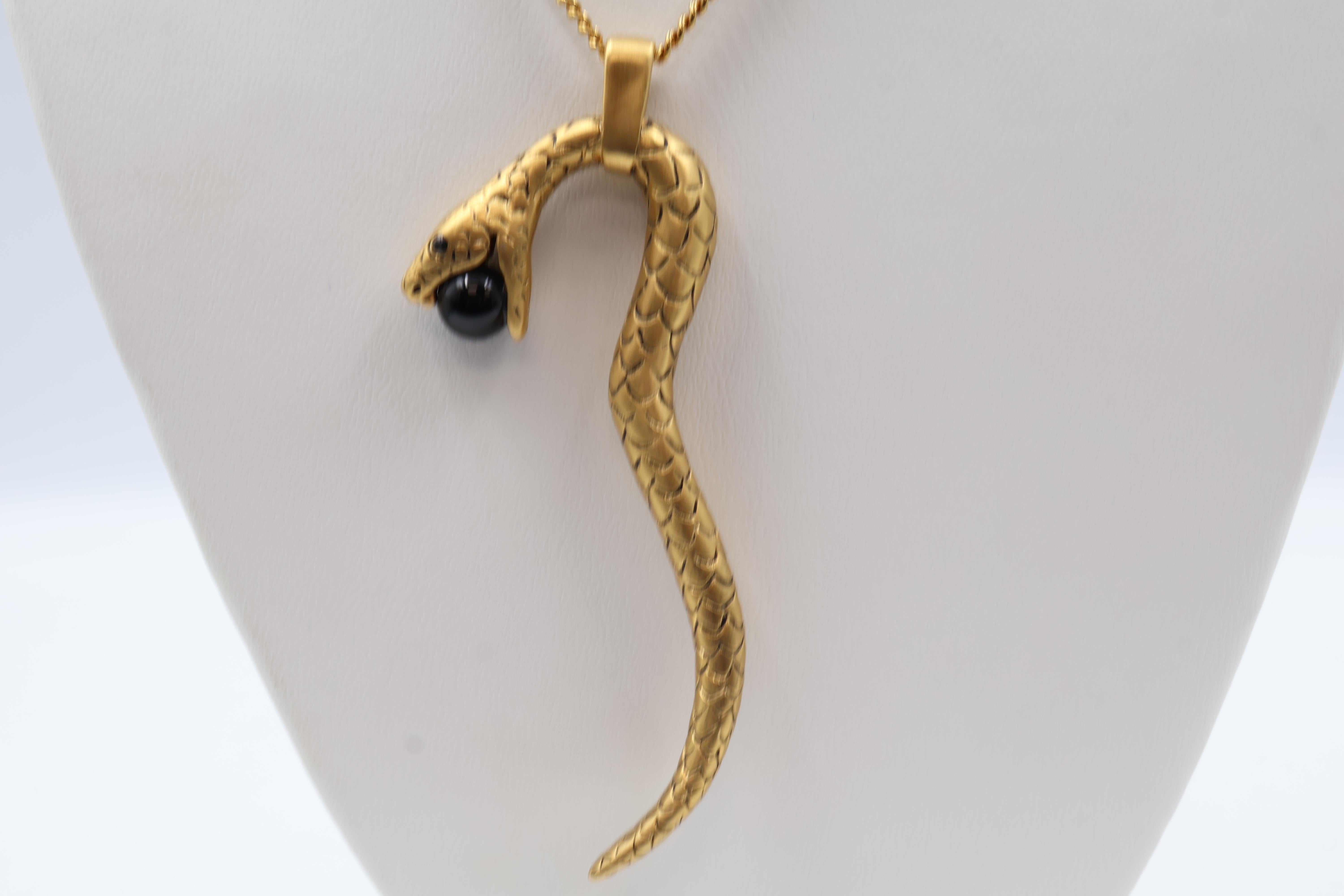 Elevate your accessory collection with the Yves Saint Laurent Gold Toned Serpent Pendant 
Chain. This exquisite necklace features a striking black glass main stone set in a yellow gold-plated body, shaped into a captivating round form. The