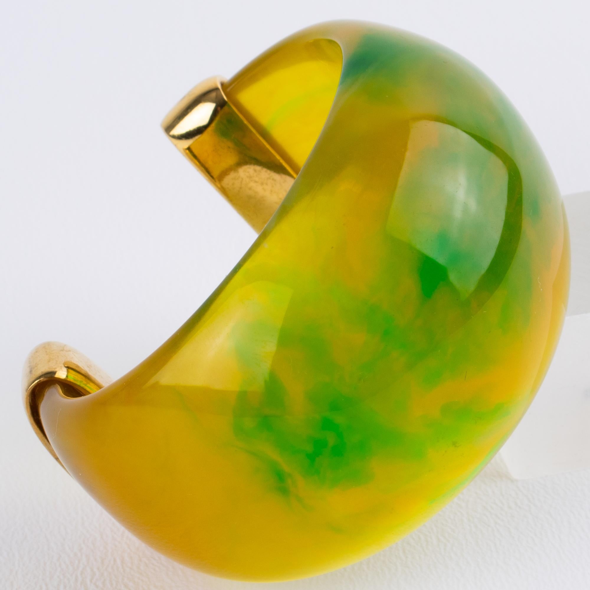 Esta exquisita pulsera brazalete YSL Yves Saint Laurent presenta un diseño grueso con forma de brazalete de Lucite o acrílico muy abombado. La pieza de moda ostenta un color amarillo calabaza translúcido jaspeado con remolinos de verde hierba y