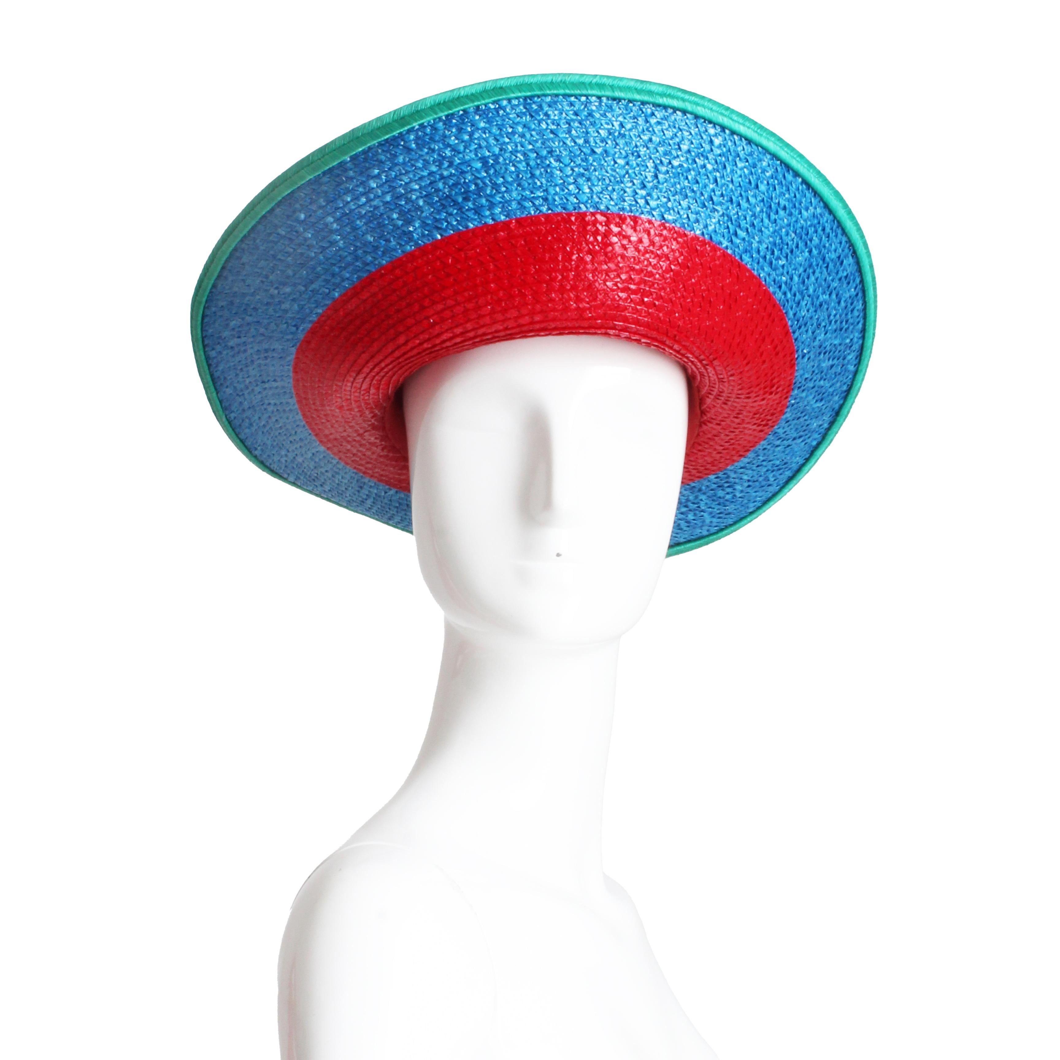 Sombrero vintage de segunda mano Yves Saint Laurent Rive Gauche, de la colección S/S '93.  Fabricada en paja con un estampado de bloques de color rojo y azul con ribete aguamarina, tiene un ala ancha estilo halo.  

La colección S/S'93 de Yves Saint