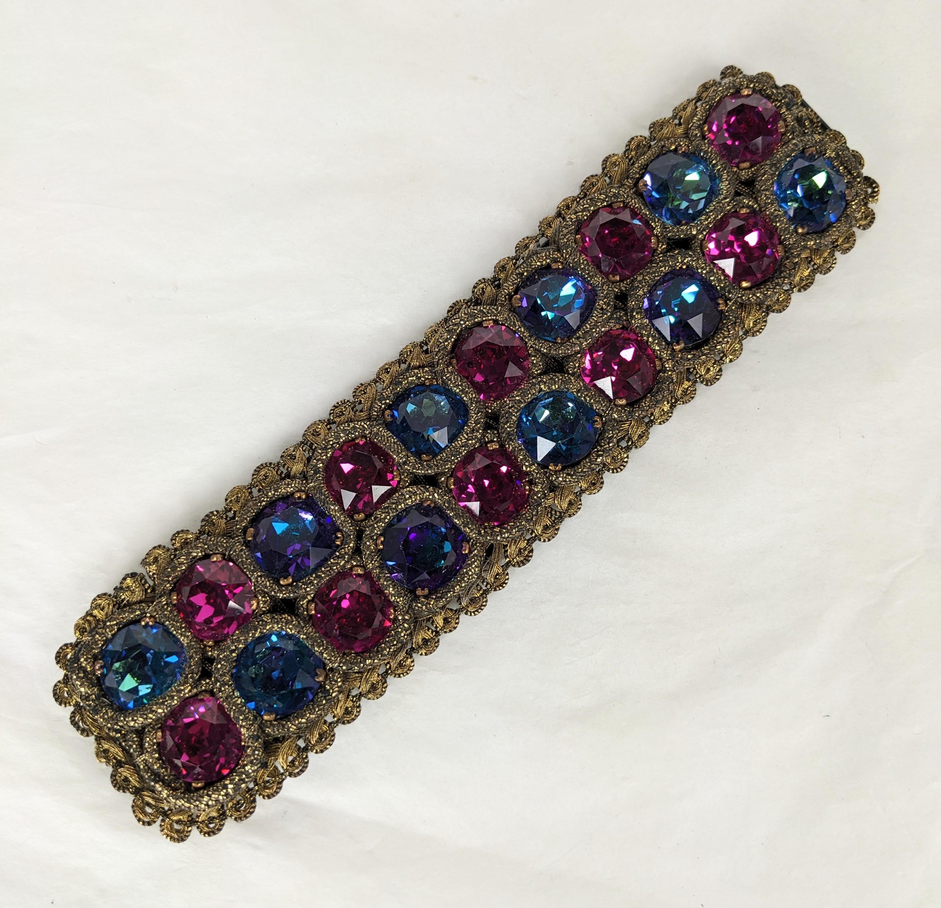 Incredibile bracciale Yves Saint Laurent Haute Couture in oro e cristalli Swarovski del 1980. Realizzato secondo la tradizione dell'Alta Moda con finiture e filati in metallo oro antico. Grandi cristalli Swarovski nei colori fuschia, blu aurora e