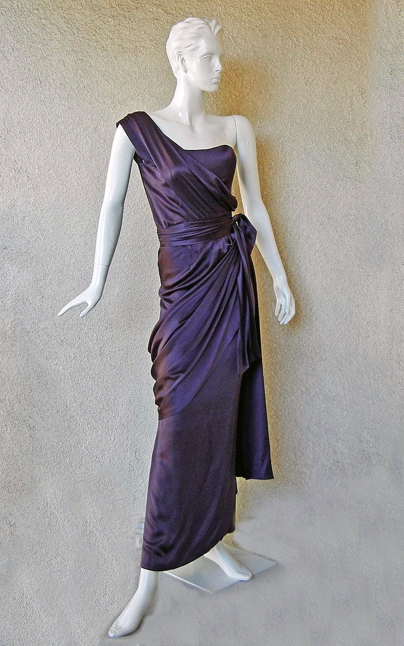 Uno splendido abito in charmeuse di seta color prugna intenso disegnato da Yves Saint Laurent dalla sua collezione Haute Couture circa 1997-98. Si ispira nello stile e nei colori al precedente design swag del designer dei primi anni '70. Monospalla