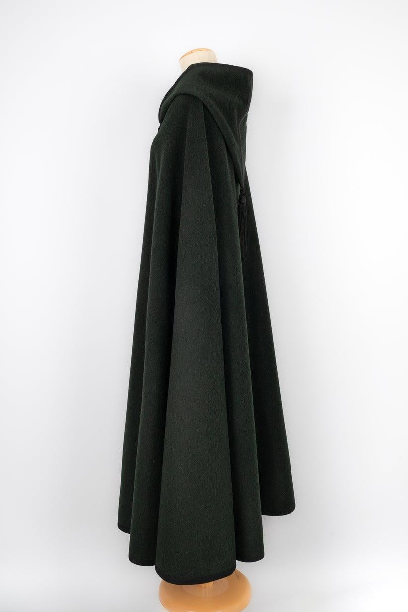 Yves Saint Laurent - (Made in France) Long dark-green wool cape with black trimmings. No size nor composition label, it fits a 36FR/38FR/40FR/42FR.

Additional information:
Condition: Very good condition
Dimensions: Length: 130 cm

Seller Reference: