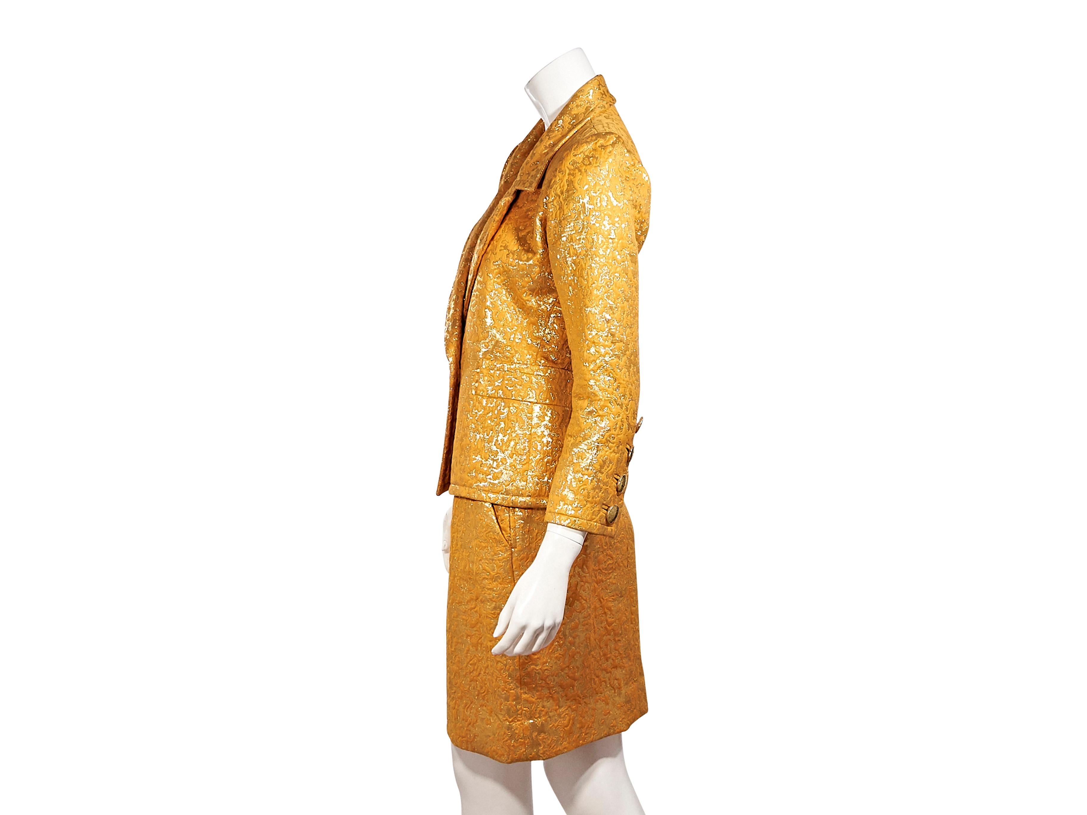Product details:  Metallic marigold cotton brocade skirt suit set by Yves Saint Laurent.  Notched lapel.  Long sleeves.  Four-button detail at cuffs.  Single-button closure.  Waist slide pockets.  Matching skirt.  Banded waist.  Goldtone hardware. 