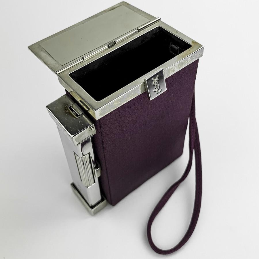 YSL minaudière in purple fabric and silver plated metal. Signed YSL on its opening button. It is rectangular and dressed in purple fabric. Initially perfectly adapted to your cigarettes and equipped with a lighter, you can carry it by hand during