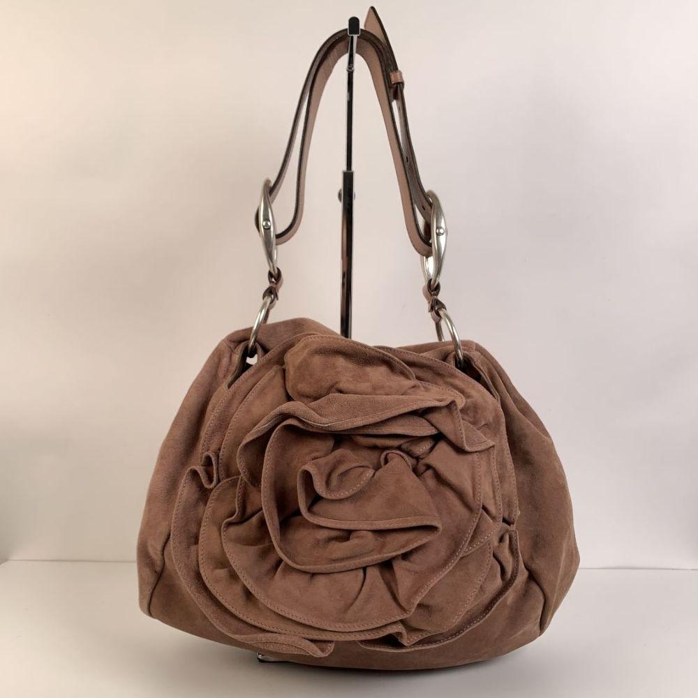Yves Saint Laurent 'Nadja Rose' Shoulder Bag, crafted in pink nude suede. It features a flap closure with a ruffled rose detail on the front and a drawstring closure. Brown suede lining. 1 side zip pocket and 1 side open pocket inside. 'Yves Saint