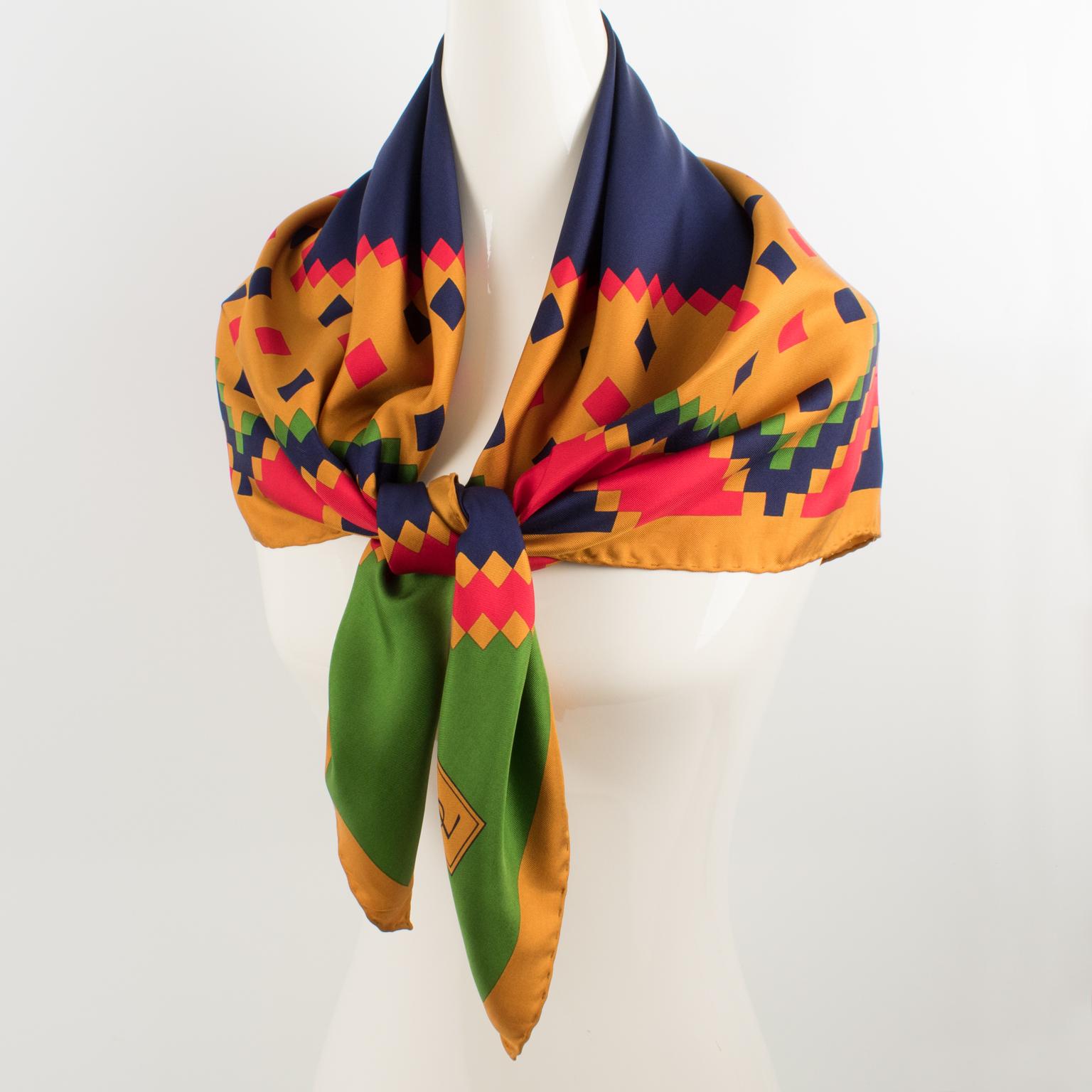 Beautiful silk scarf by Yves Saint Laurent Paris in assorted colors featuring a geometric design print with a YSL signature on the bottom left corner. The colors are bright and vibrant with a combination of navy blue, bright red, and crocodile green