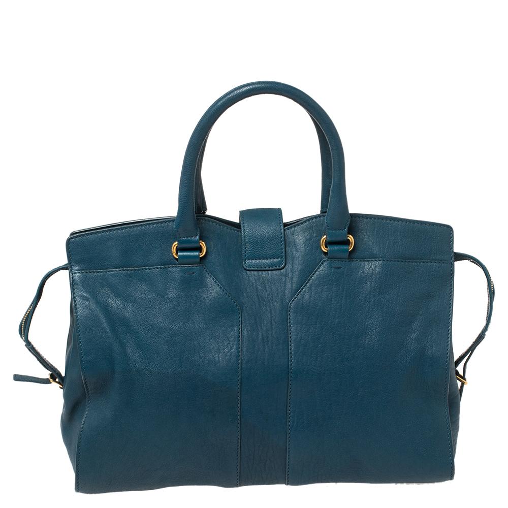 This classy Cabas Chyc tote coming from Yves Saint Laurent Paris will adorn your look in the most stylish ways. It is crafted from leather in a teal blue hue, featuring two rolled handles and zip-up closure. This tote comes with a fabric-lined
