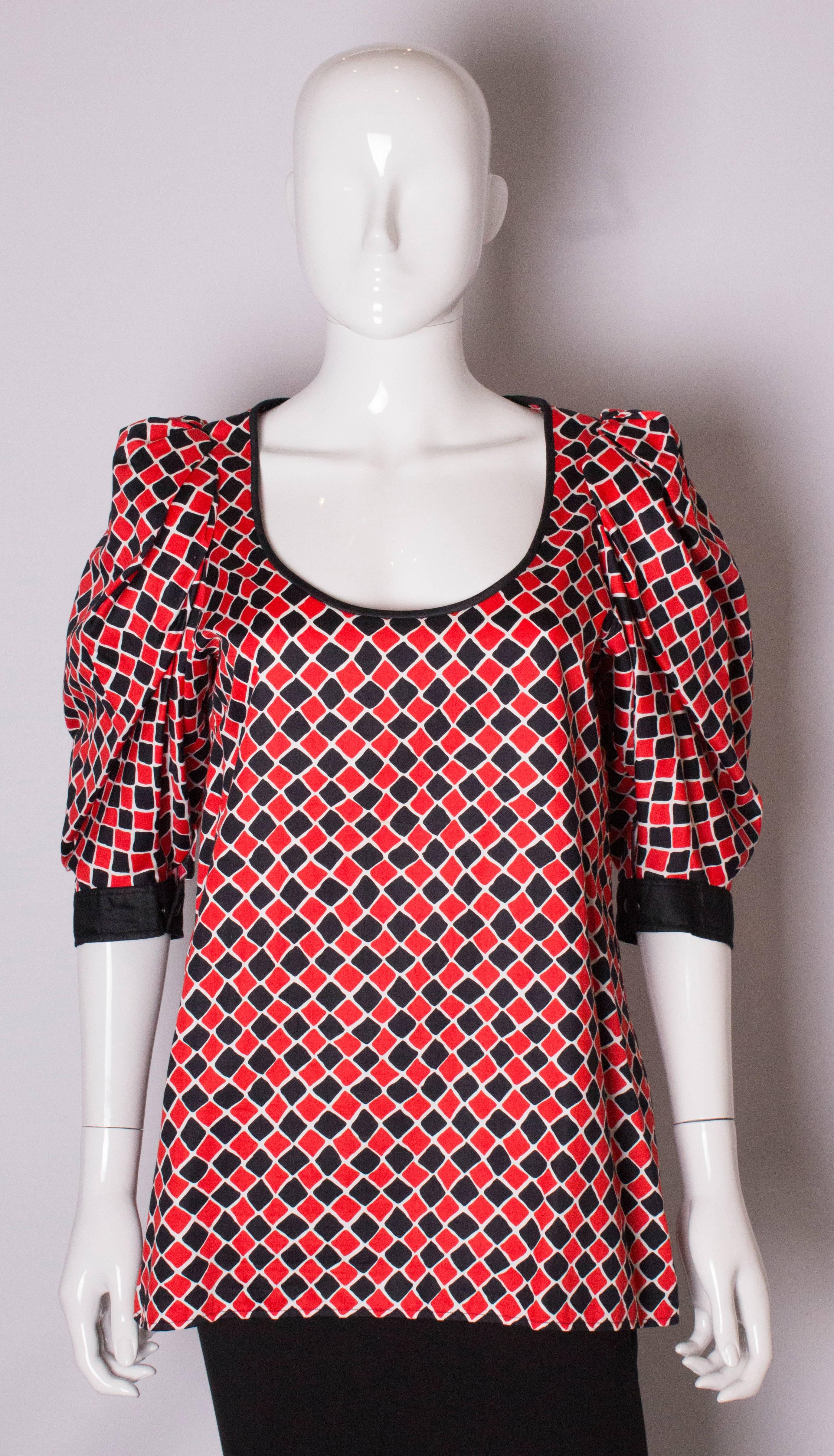 A chic and easy to wear top by Yves Saint Laurent, Rive Gauche. The top has a scoop neckline, a white background with a black and red diamond print, black edging, and elbow length sleeves with double buttons.