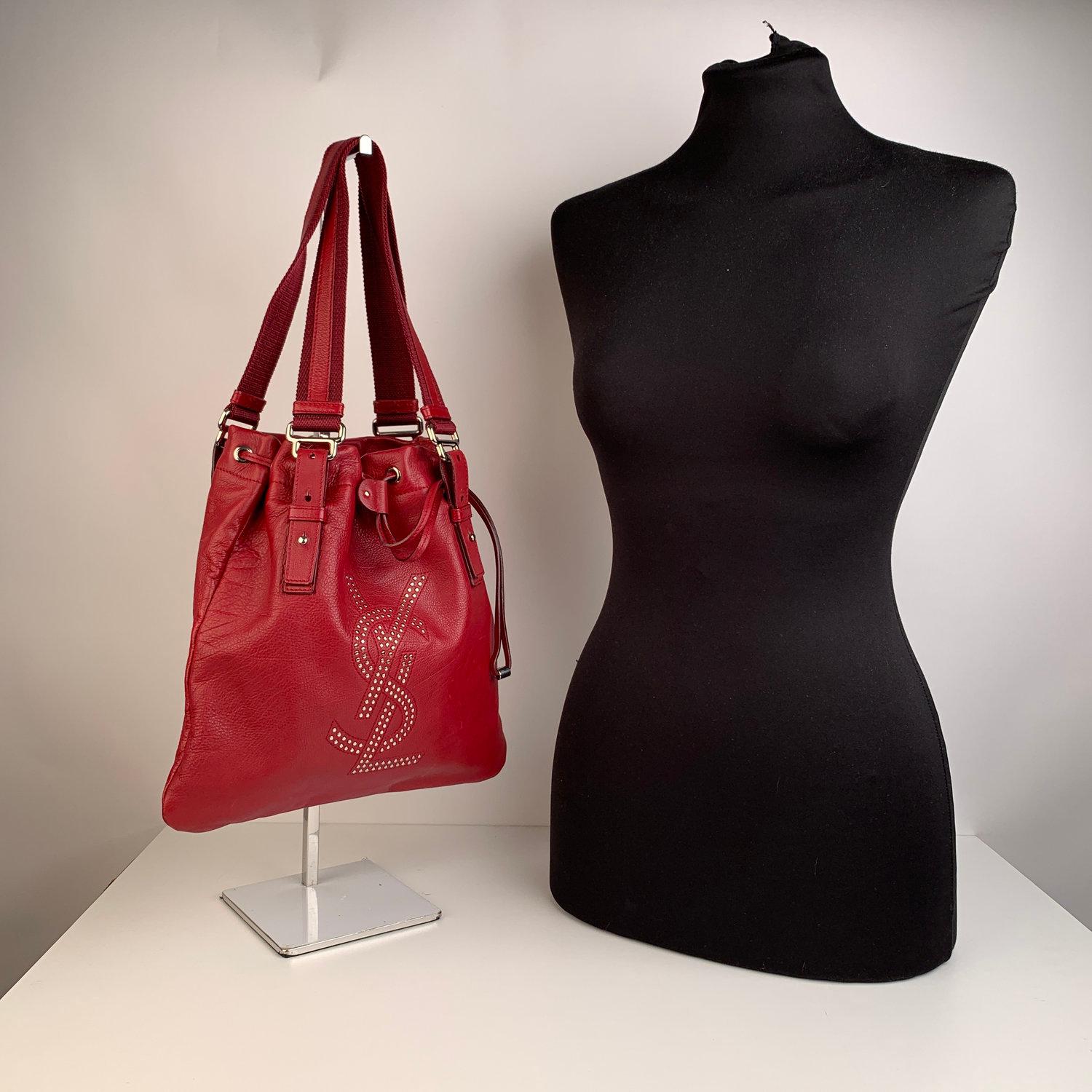 YVES SAINT LAURENT red leather 'Kahala Sac' tote bag, with silver metal studded YSL logo on the front. Drawstring closure on top. Double canvas and leather handles/straps. Black satin lining. 1 side zip pocket inside. 'YVES SAINT LAURENT Rive