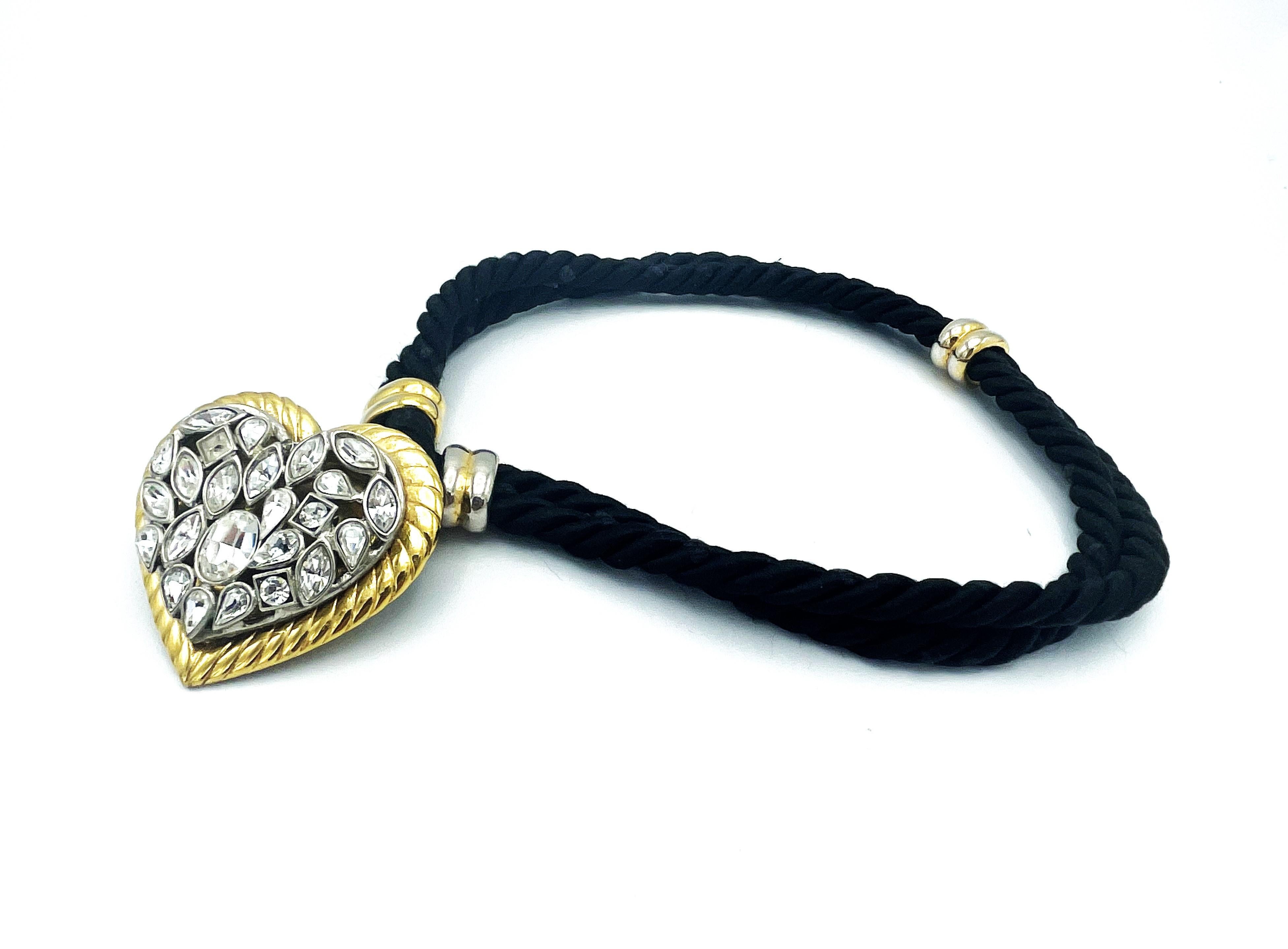 Very nice heart in gold with a cord edge. A silver heart is attached to it, which is filled with differently cut rhinestones. A double black cord is attached to the back of the heart and the chain can be worn short or long. A very rare decorative