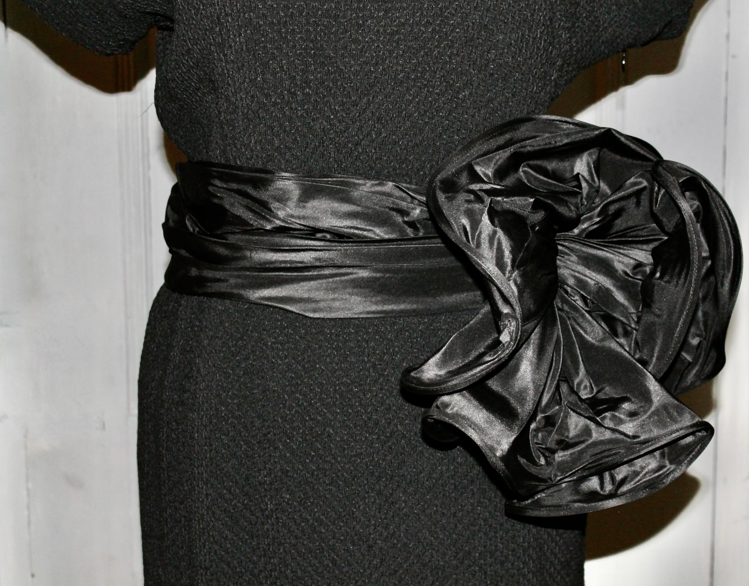 A beautiful YSL Rive Gauche Paris, France black cocktail dress, with a silk belt with a large flower bow. Shoulders are lightly padded.  Zipper on side, button at neck opening in back. Acetate, rayon and silk. Size EU 40. 