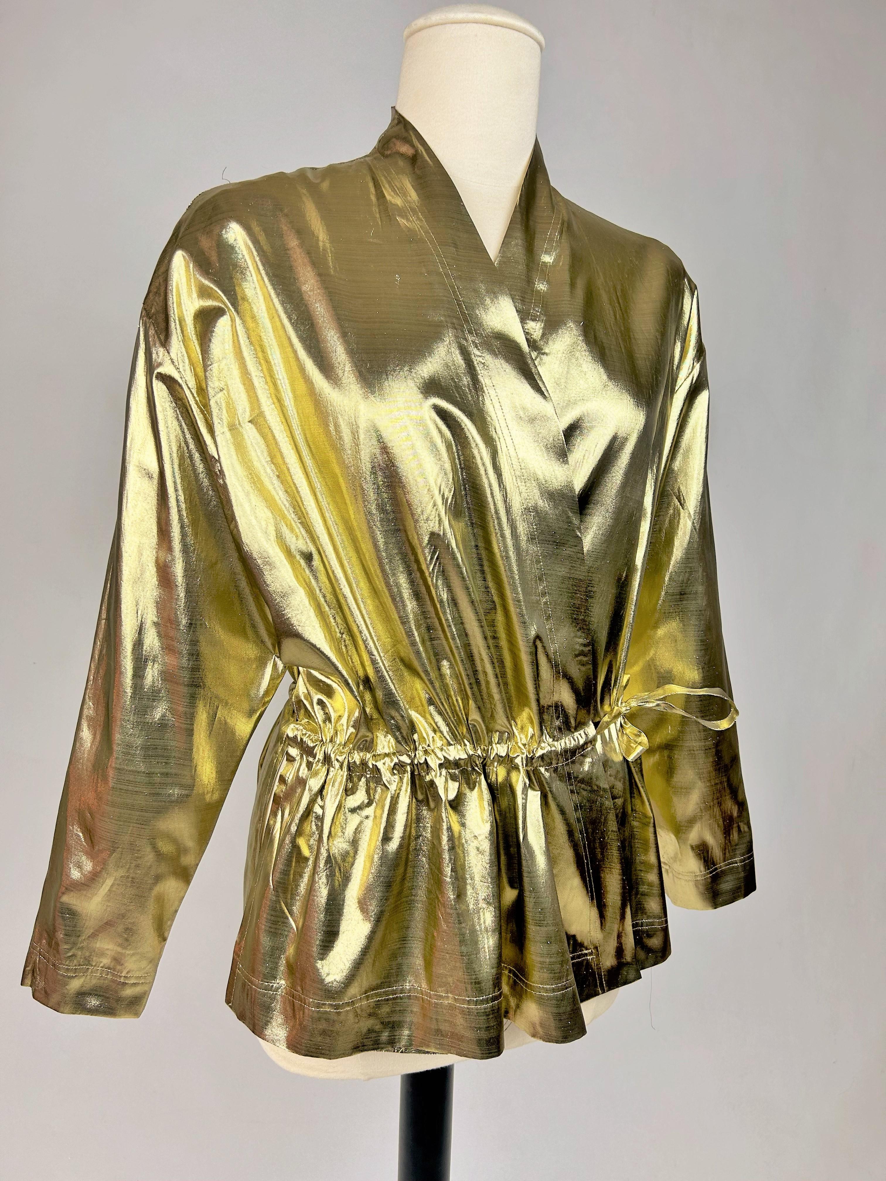 Circa 1990
France
Kimono blouse in very fine gold lamé by Yves Saint laurent Rive Gauche dating from the 1990s. Wide, flowing cut, slit on the sides and crossed at the front by a thin, matching sliding belt, allowing it to be tied at the waist. No
