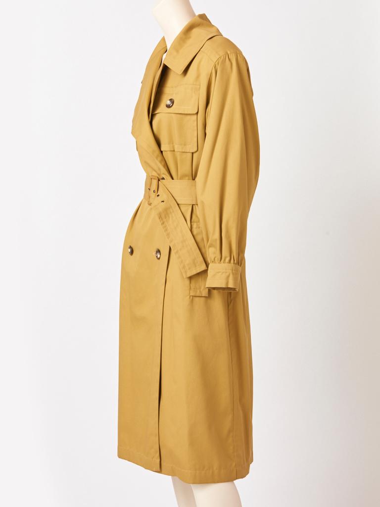 Yves Saint Laurent, Rive Gauche, khaki tone, double breasted, cotton, belted trench, having wide lapels, breast pockets, slash, side pockets and a deep back middle vent. Sleeves gather slightly at the cuff. Interior is lined in a heavy cotton.
