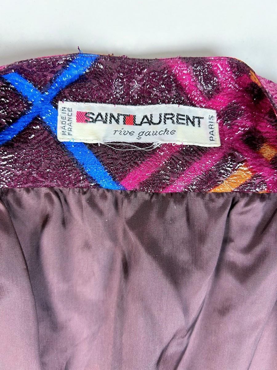 Um 1990

Frankreich

Lurex-Lamé-Cocktailkleid von Yves Saint Laurent Rive Gauche aus den 1990er Jahren. Vorne offenes Wickelkleid mit gekreuztem Gürtel, der einen tiefen V-Ausschnitt ermöglicht.  Blusiger, schulterfreier Schnitt mit langen Ärmeln