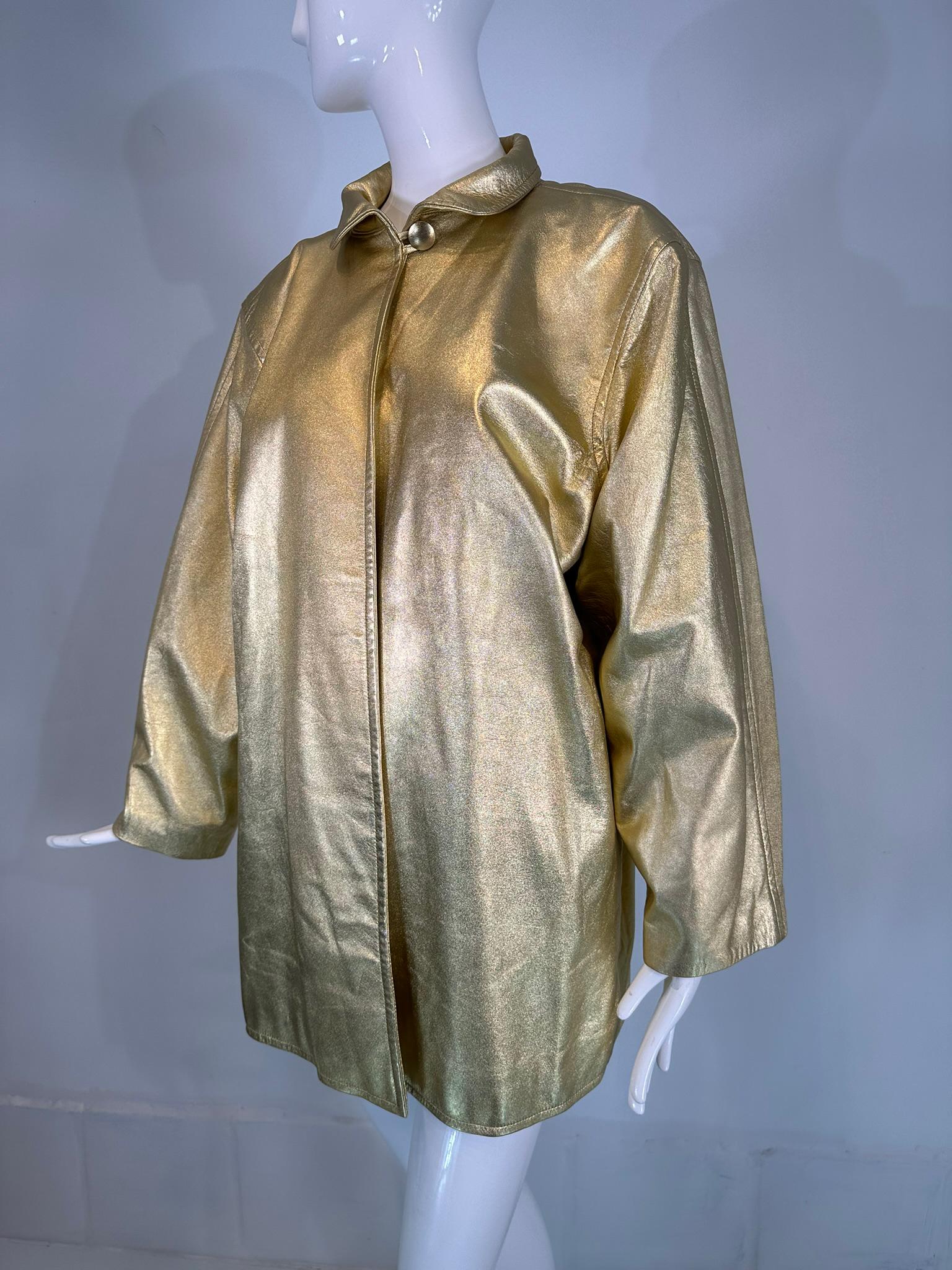 Giacca in pelle dorata Yves Saint Laurent Rive Gauche degli anni '80. Giacca oversize con fodera in nylon nero trapuntato. La giacca si chiude al collo con un singolo bottone dorato e un passante, sotto il colletto rotondo. La giacca ha le spalle