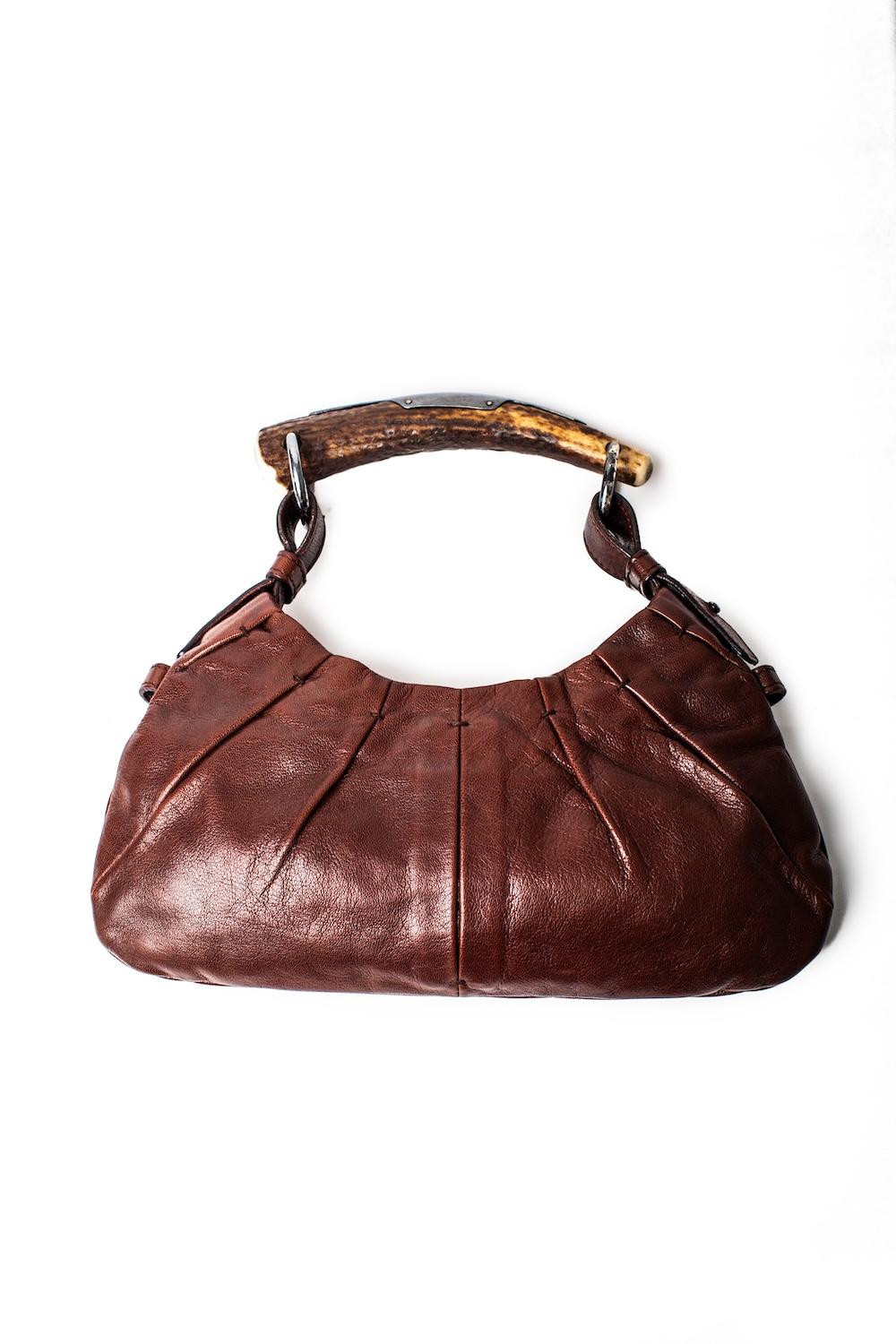 Dating to the S/S 2002 collection designed by Tom Ford, this Mombassa bag by Yves Saint Laurent is made from distressed chestnut leather with a silver embellished horn handle. Fully lined in brown suede, this closes with a magnetic button closure