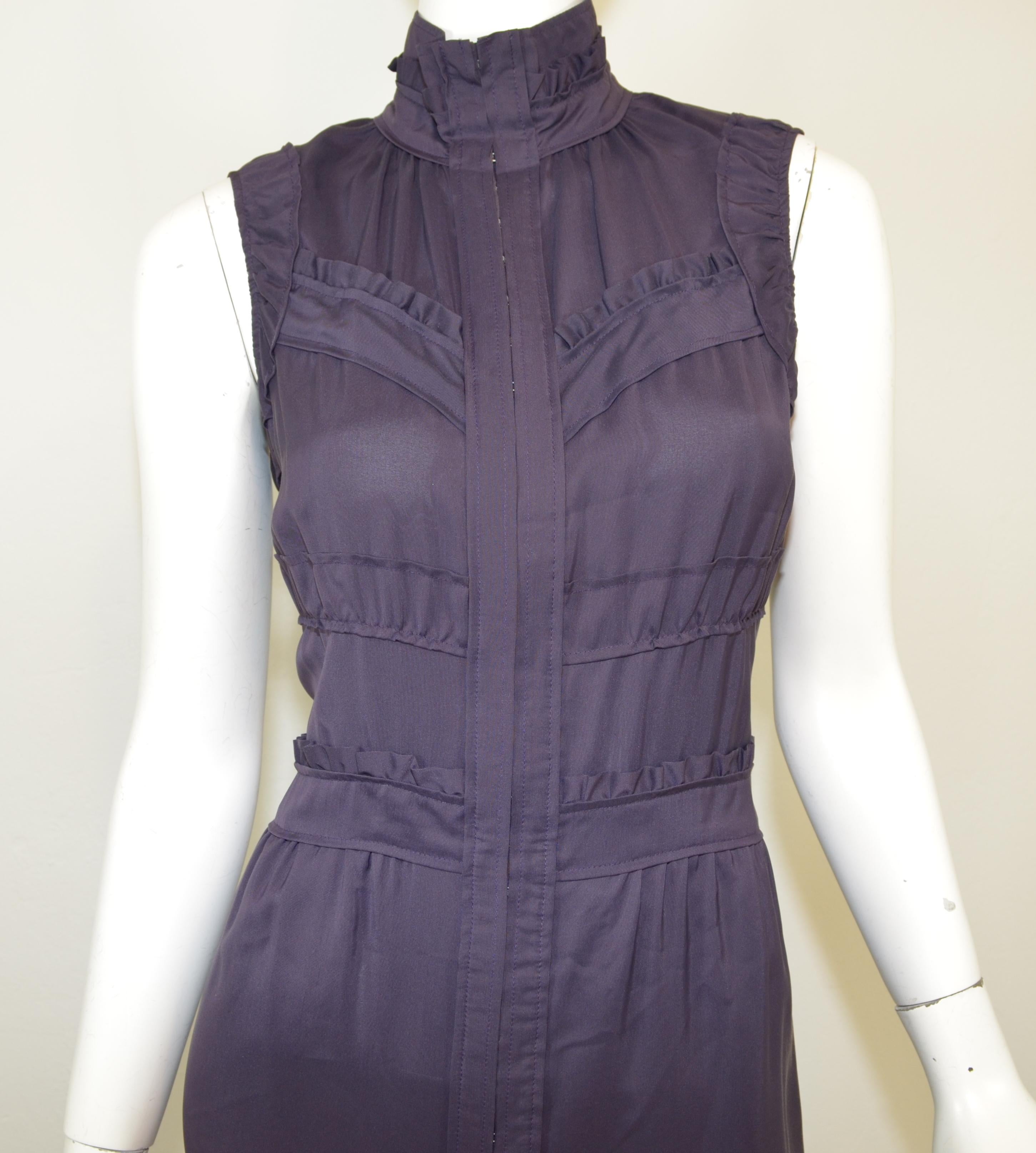 Yves Saint Laurent dress is featured in a dark purple, eggplant color with a mock neckline, ruffle detail trim, pockets at the hips, and hook-and-eye fastenings along the front center. Dress is composed with a silk and viscose blend, size 40, and is